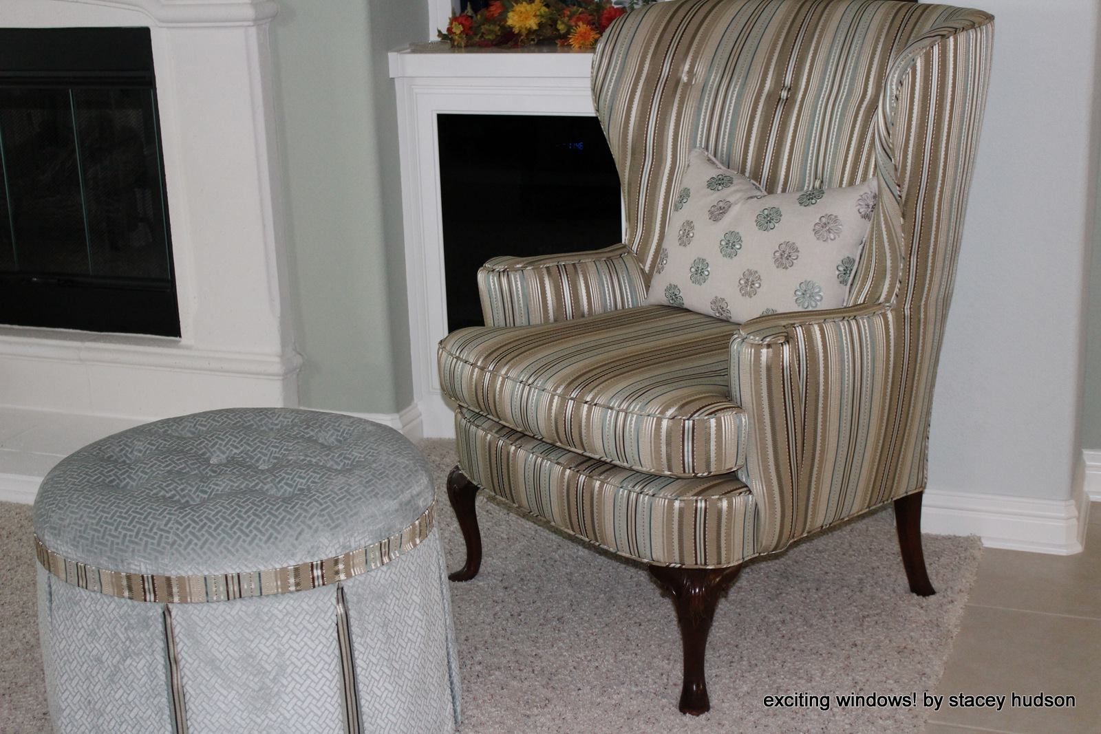 A chair and ottoman are in a living room in front of a fireplace.