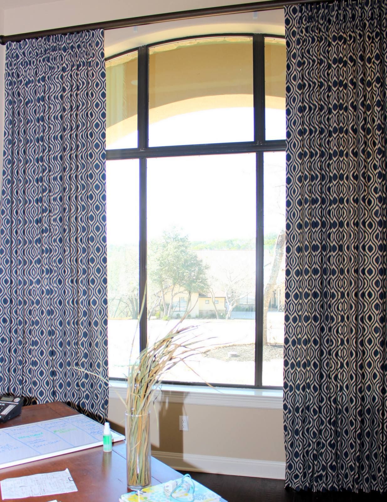 A room with a desk and a large window with blue curtains