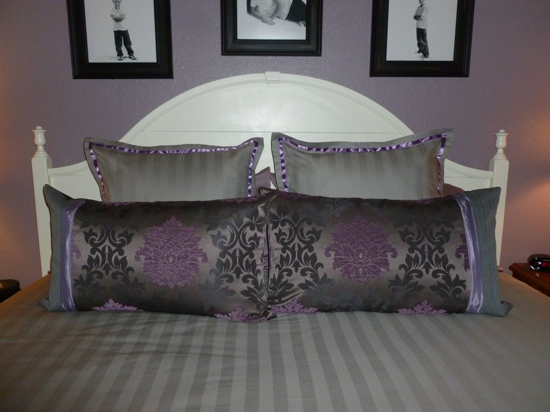 A bed with purple and grey pillows and a white headboard