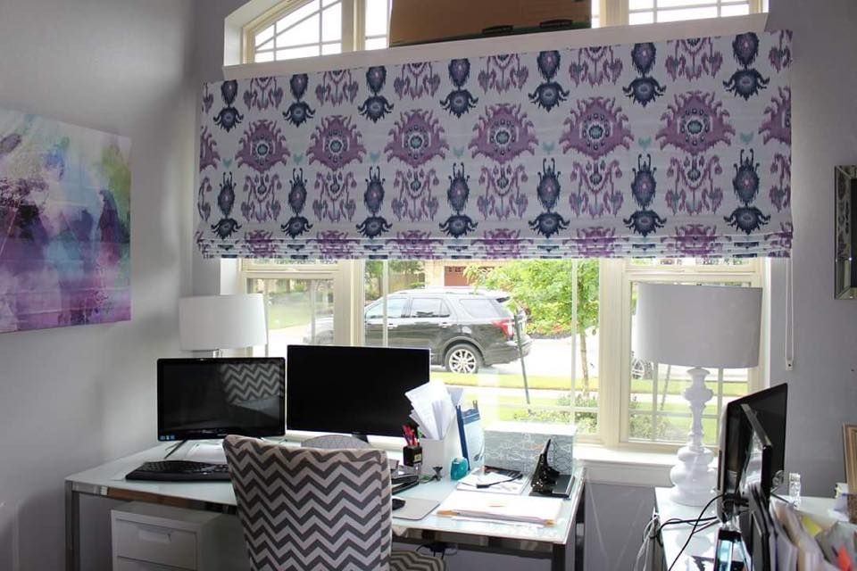 A home office with a purple roman shade on the window.