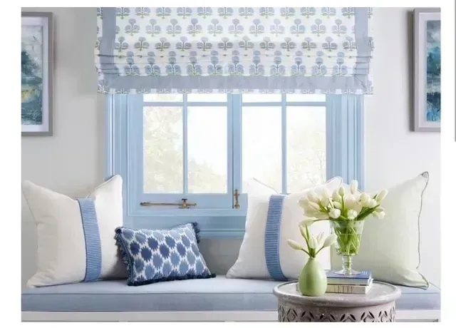 A living room with a window seat filled with pillows and a vase of flowers.