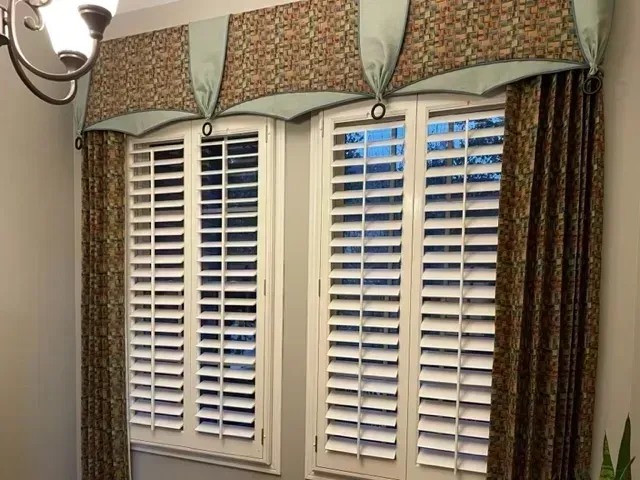 There are two windows with shutters and curtains in the room.