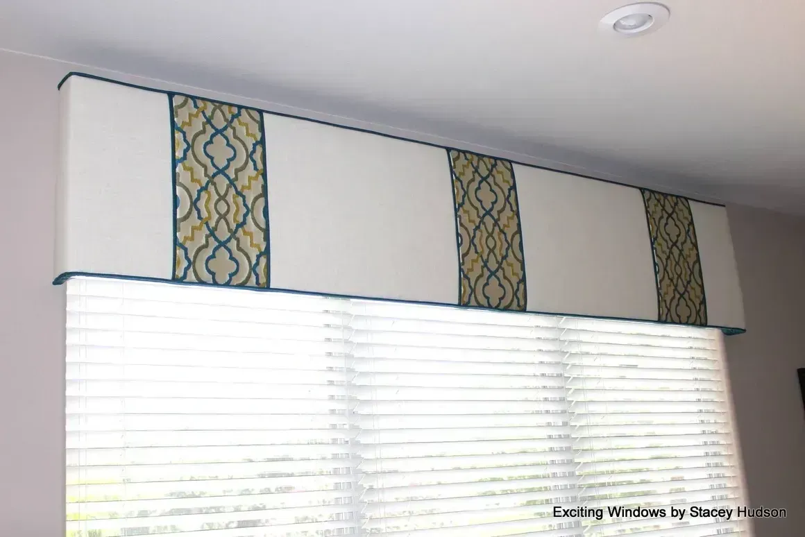 A window with blinds and a valance hanging from the ceiling.