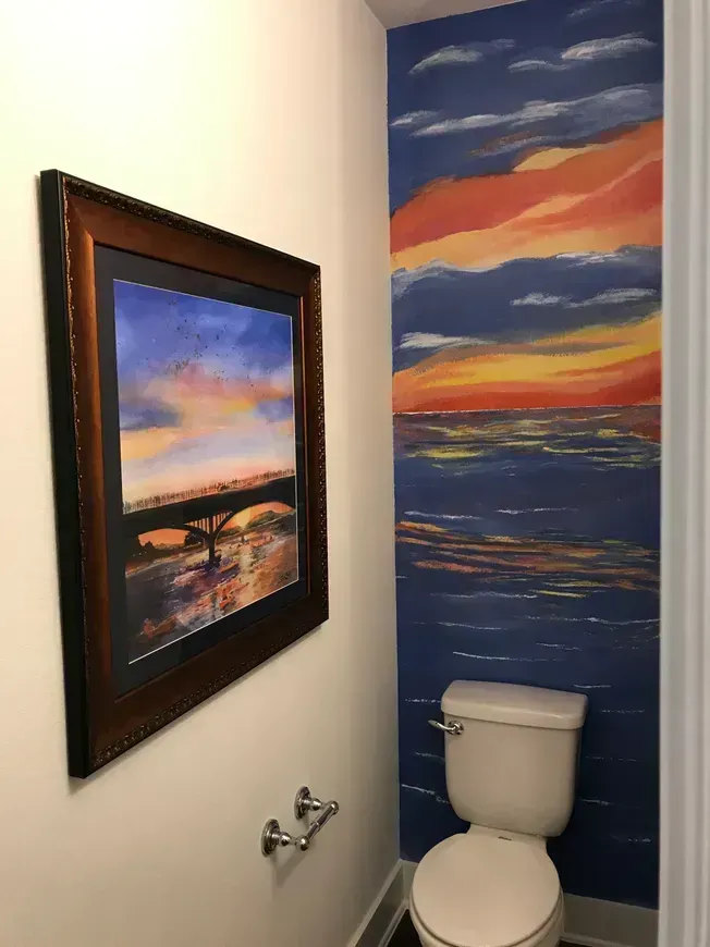 A bathroom with a painting on the wall above the toilet