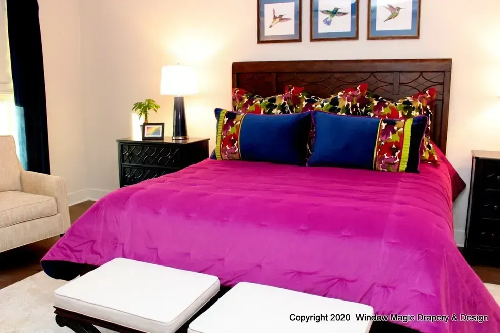 A bedroom with a purple bed , blue pillows , and a couch.