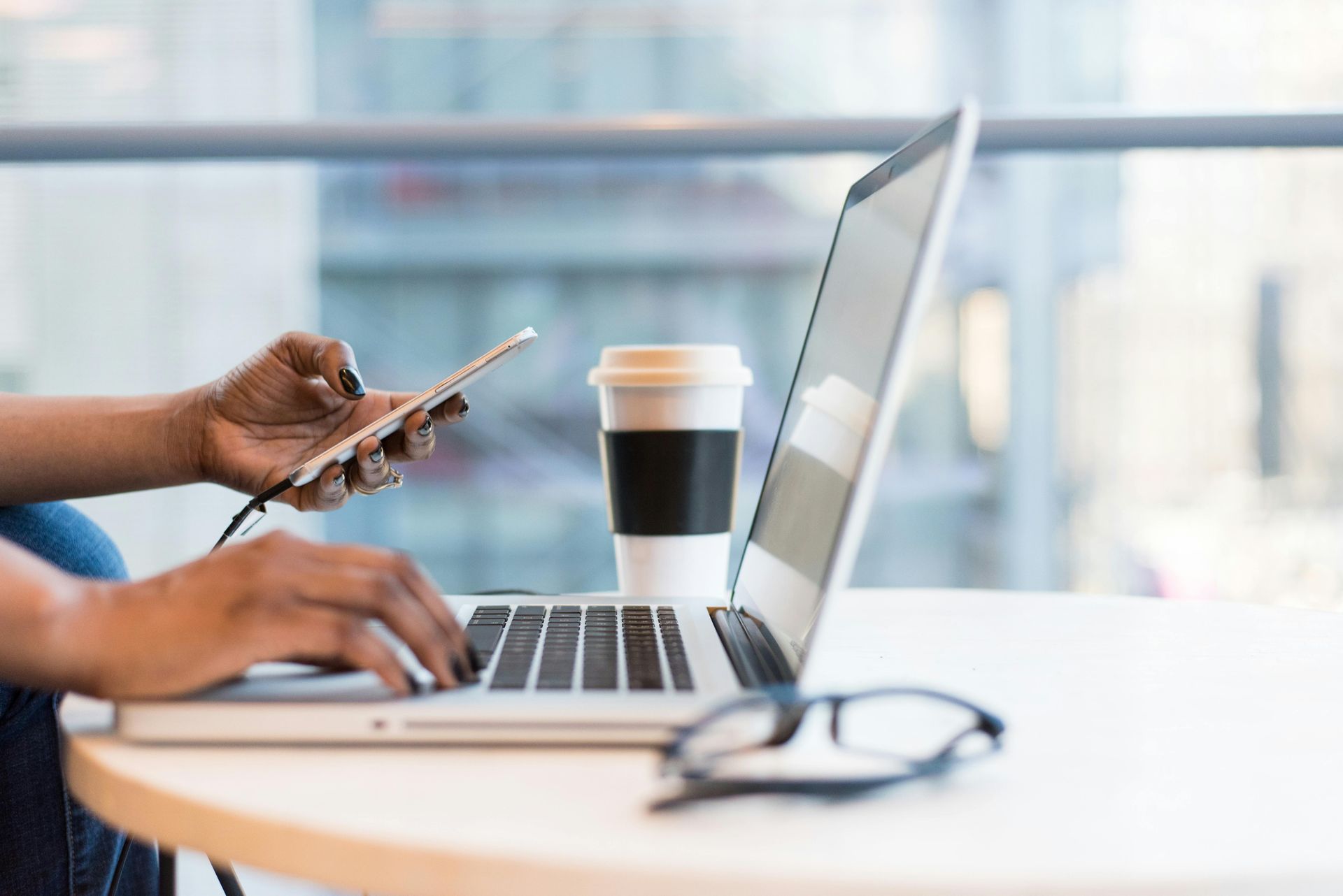 A person is sitting at a table using a laptop and a cell phone.