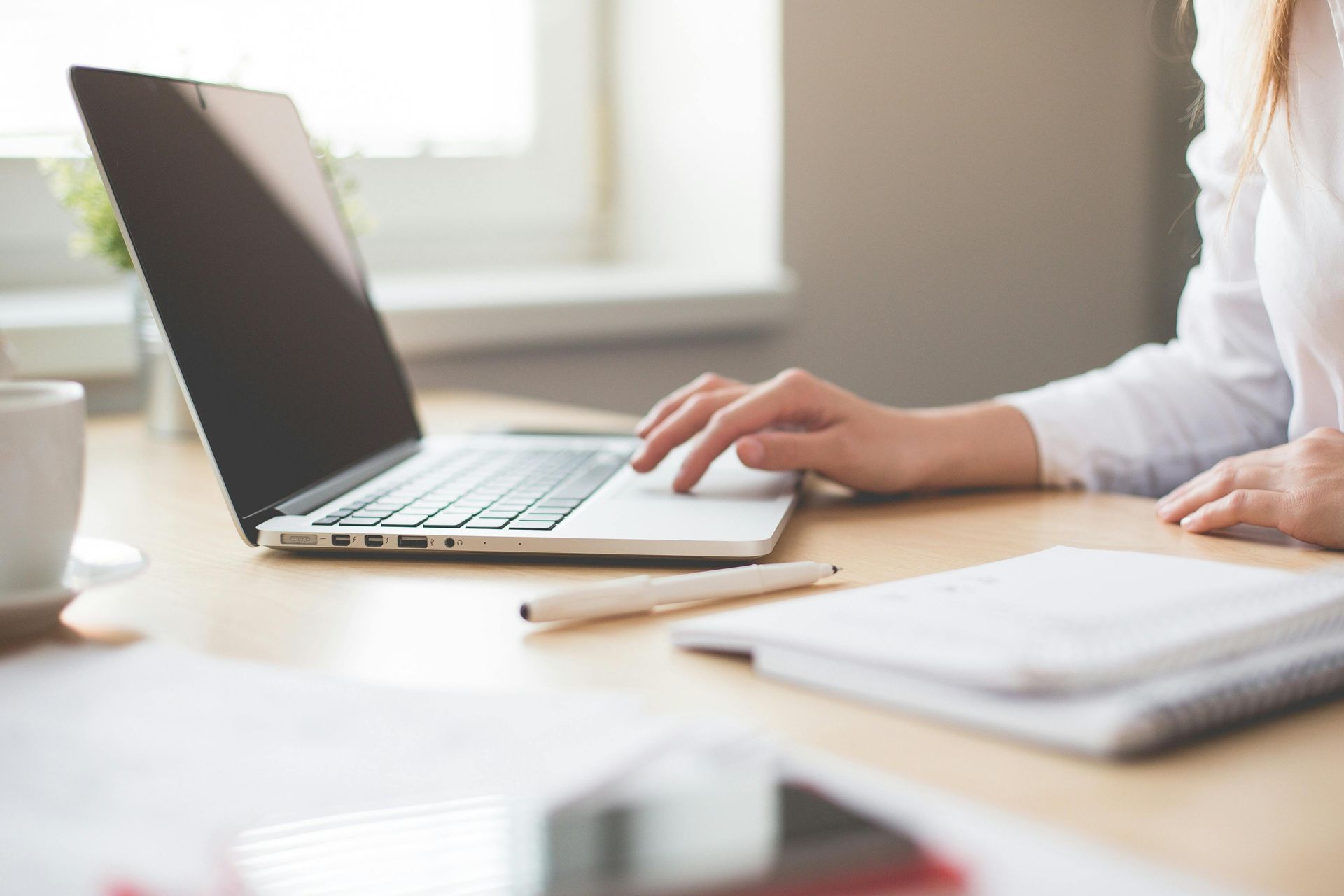 A woman is typing on a laptop computer at a desk.