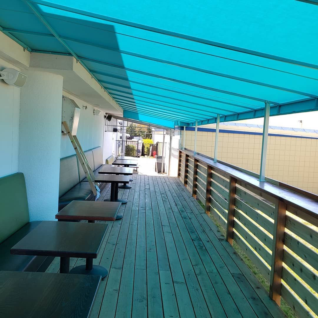 A wooden deck with tables and chairs under a blue awning