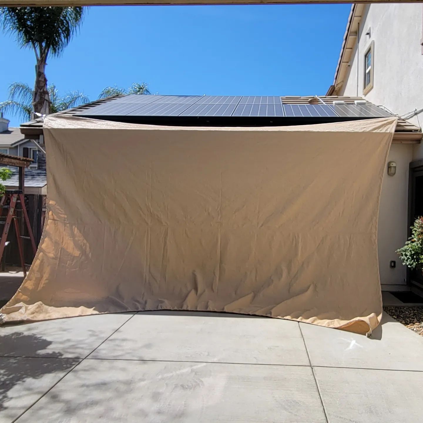 A large tan tarp is covering a house with solar panels on the roof
