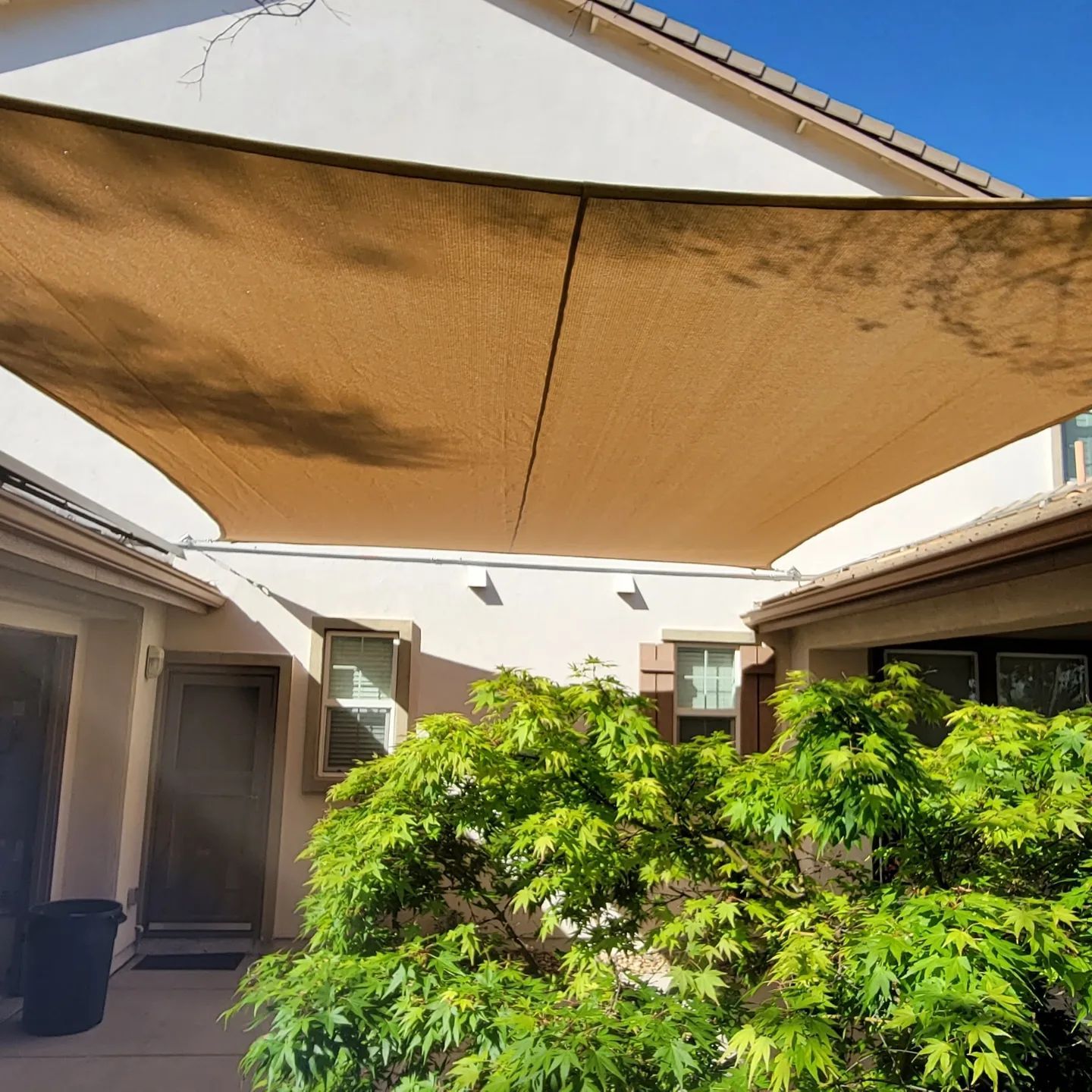 A large shade sail is covering a tree in front of a house.