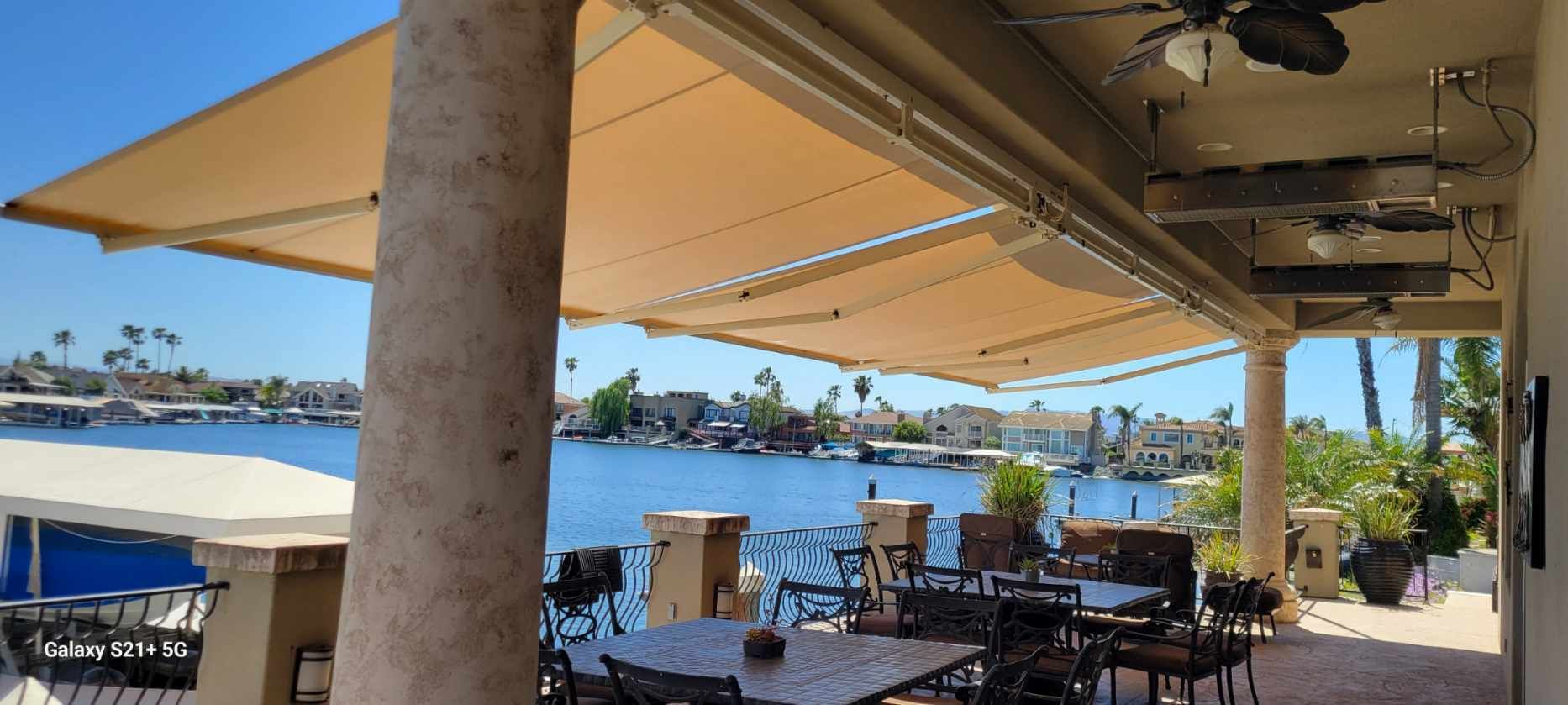 A patio with tables and chairs under an awning overlooking a body of water.