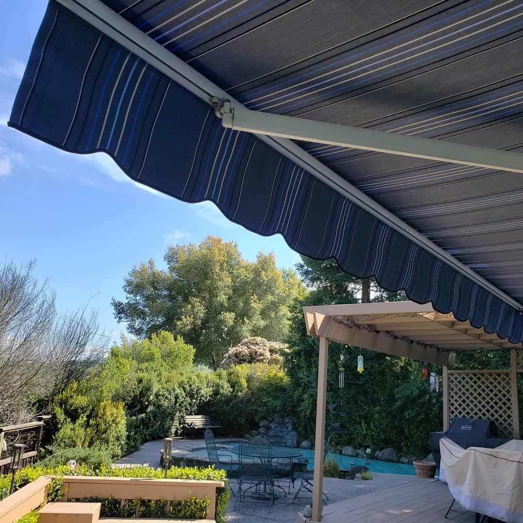 A blue awning is covering a patio with a swimming pool in the background.