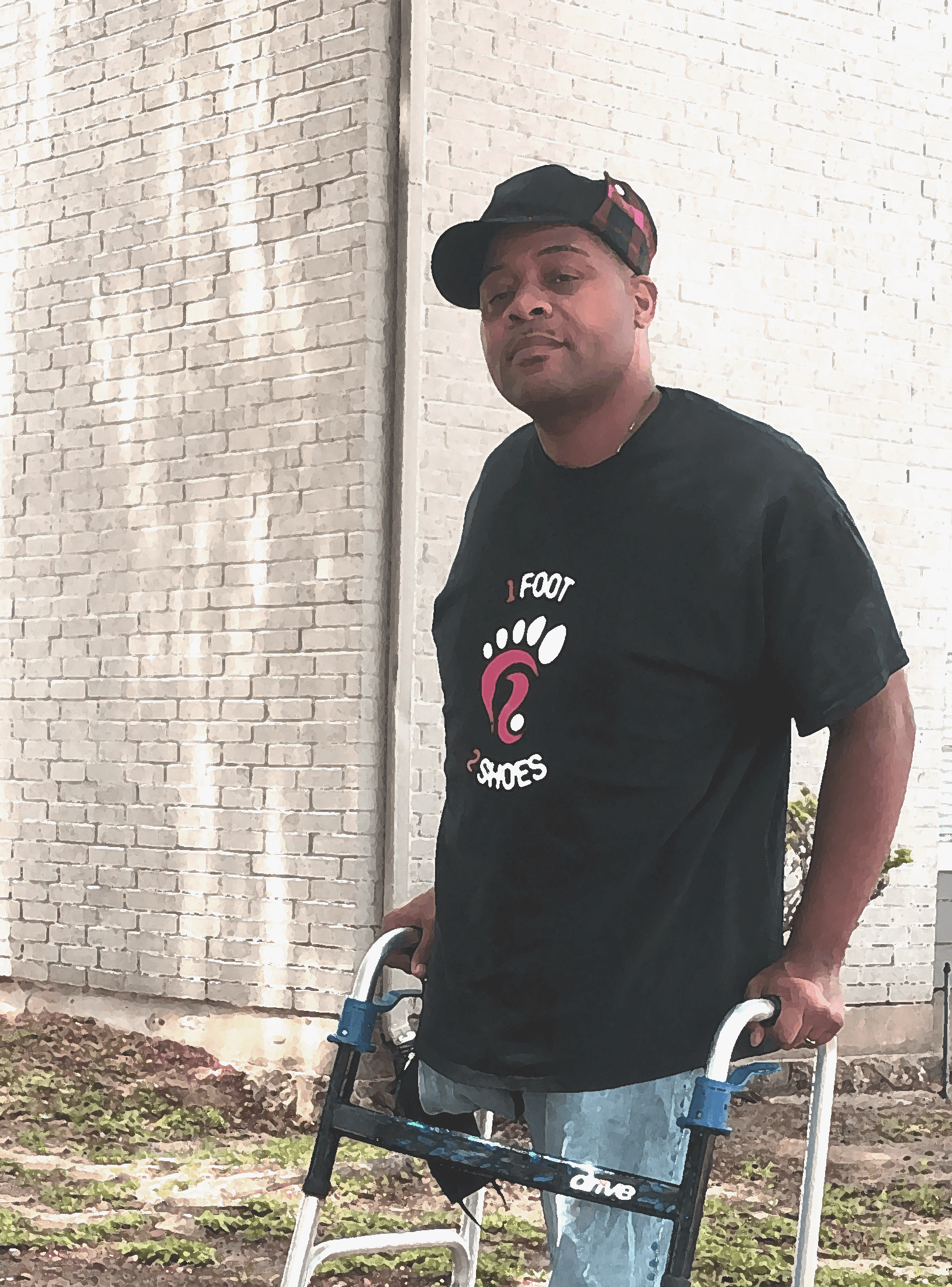 Picture of Nijo Shaw with a grin facing the camera. He wears his branded t-shirt and some jeans while standing on his walker.