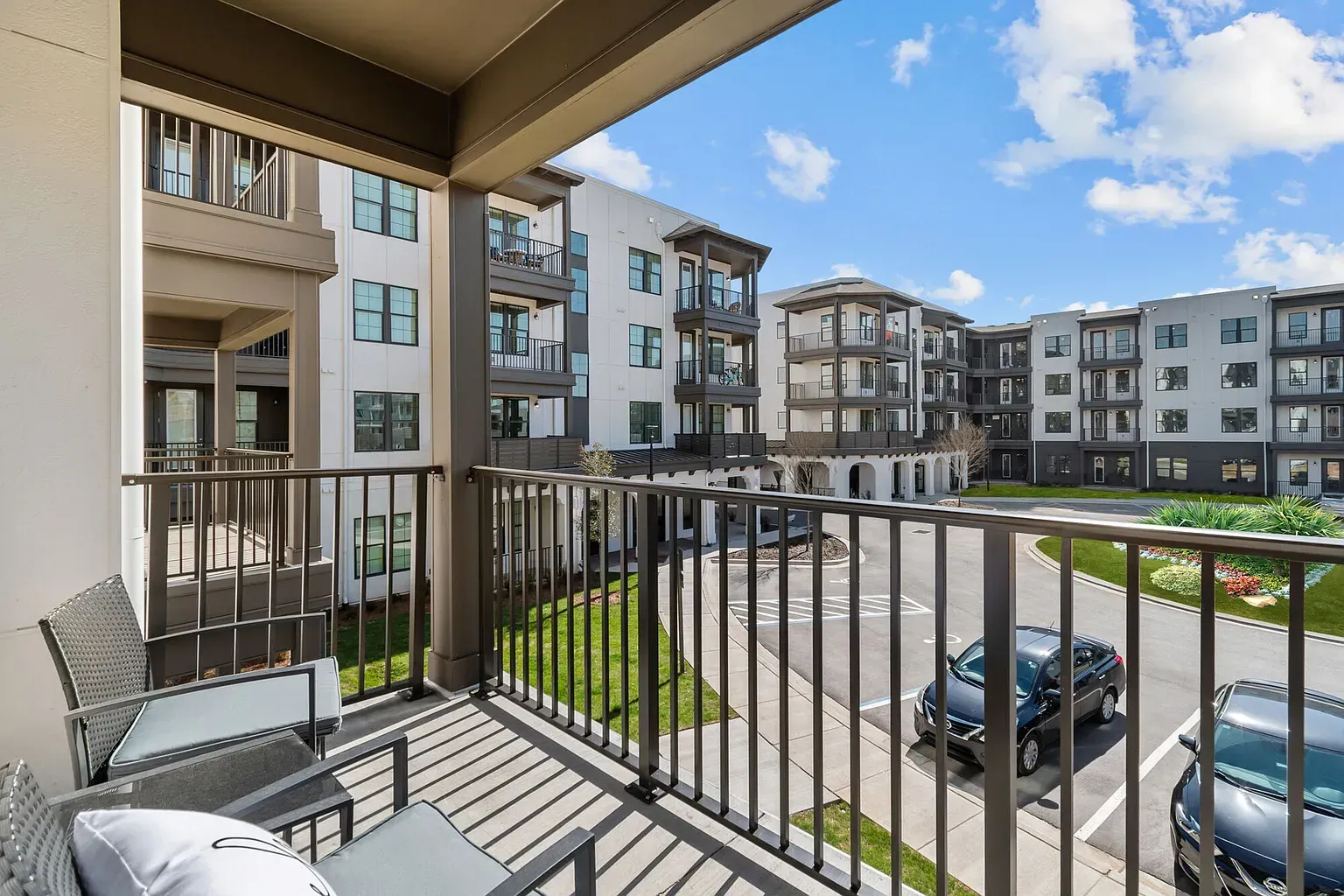 View from a balcony of a modern apartment complex courtyard with balconies, greenery, and parked cars.