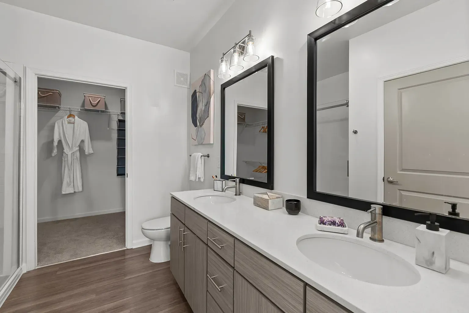 Dual-sink bathroom vanity with large framed mirrors; closet visible through doorway.