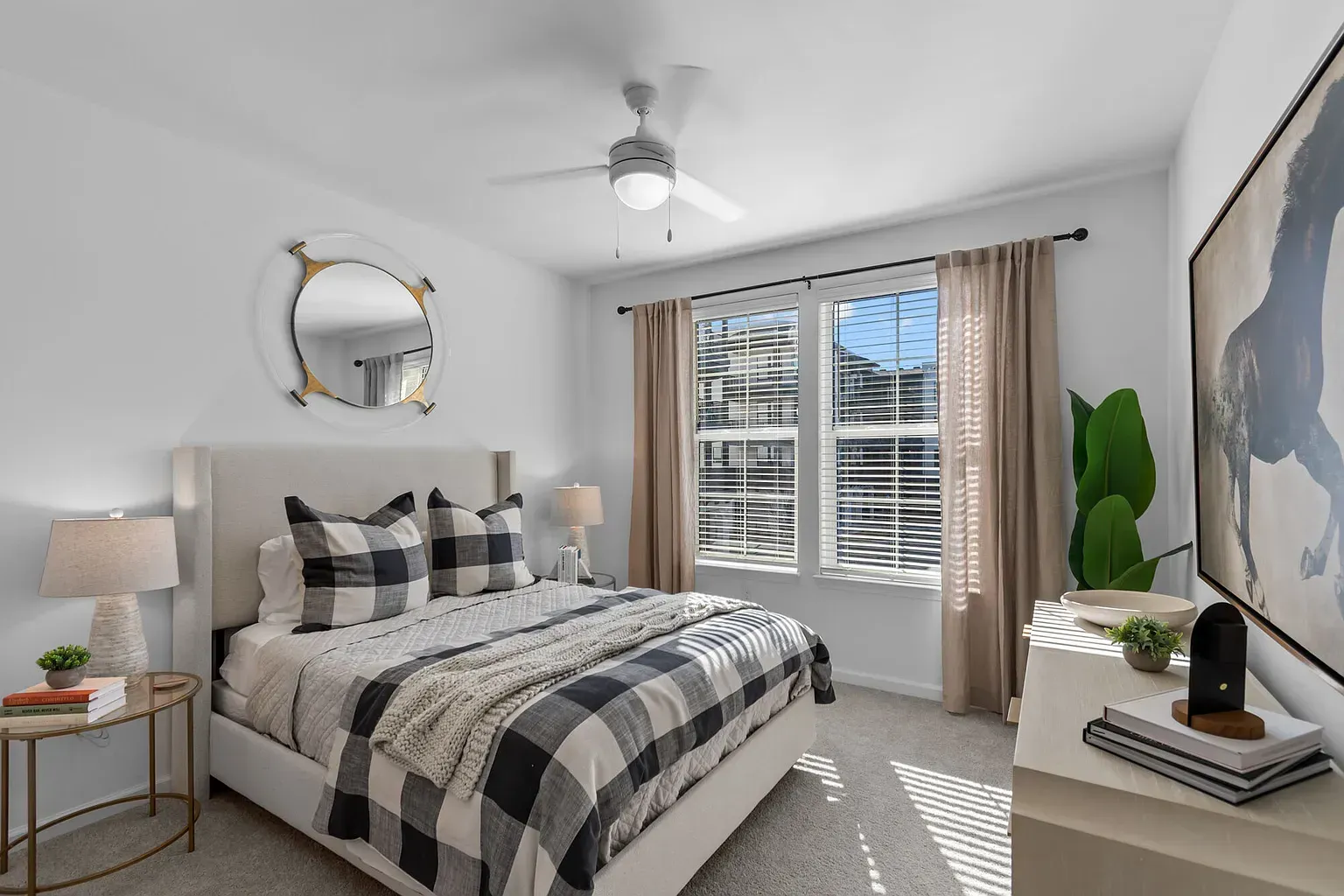 Bedroom in an apartment with a bed, plaid bedding, nightstands, and a large window.