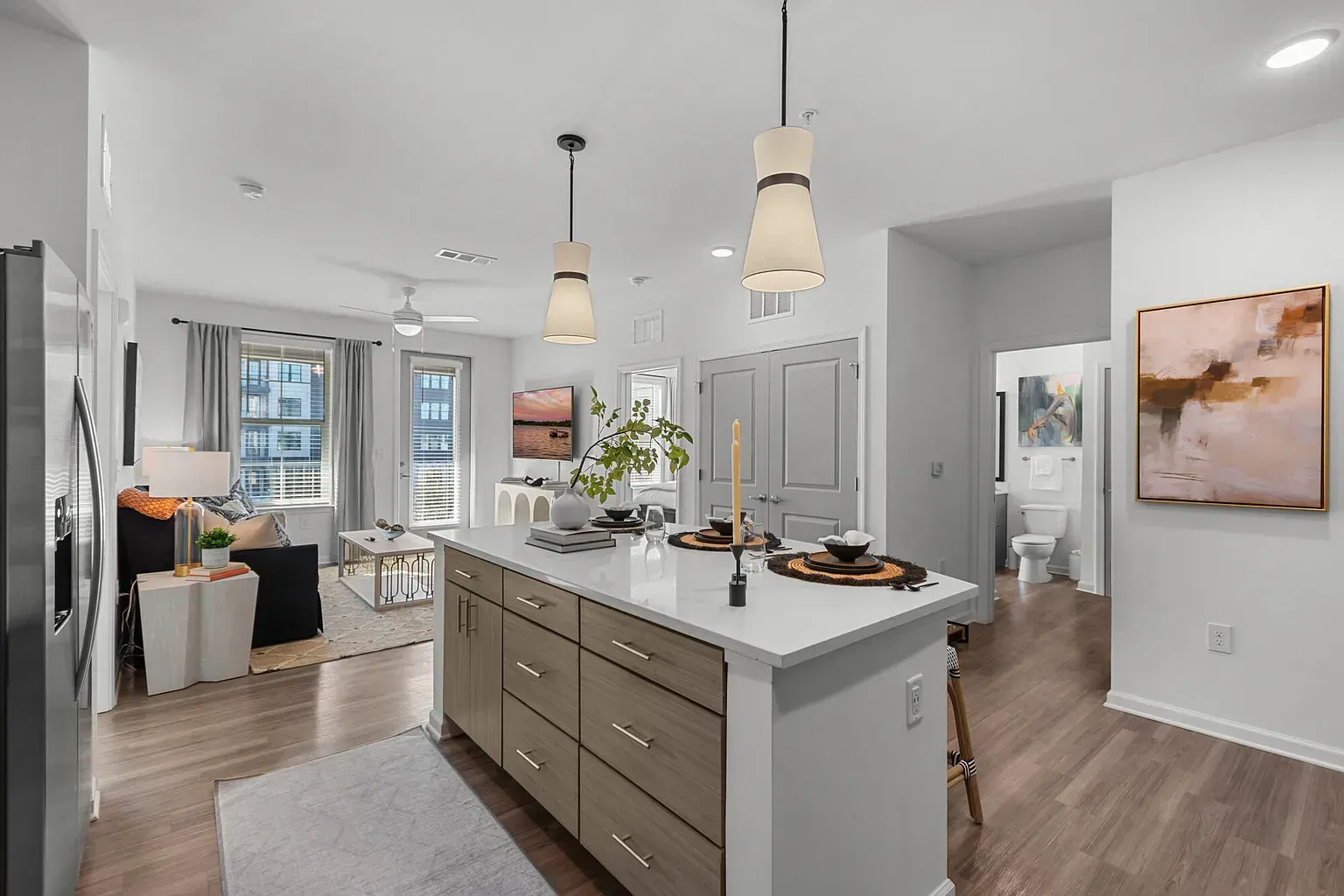Open-concept apartment kitchen with island, pendant lights, and a living area with windows.