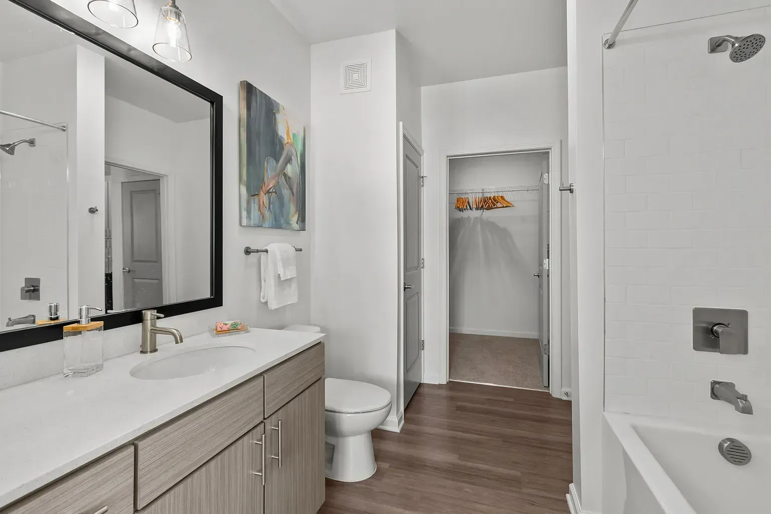 Modern apartment bathroom with vanity, mirror, toilet, tub/shower, and open closet.