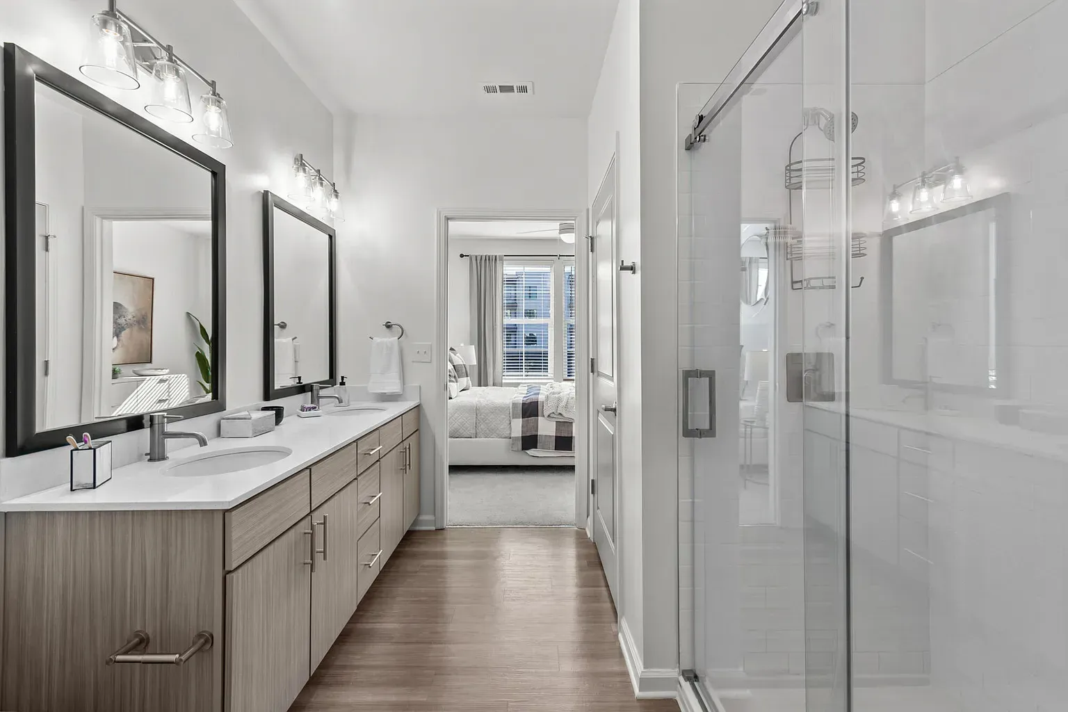 Double-sink bathroom vanity with a glass-enclosed shower in a modern apartment unit.