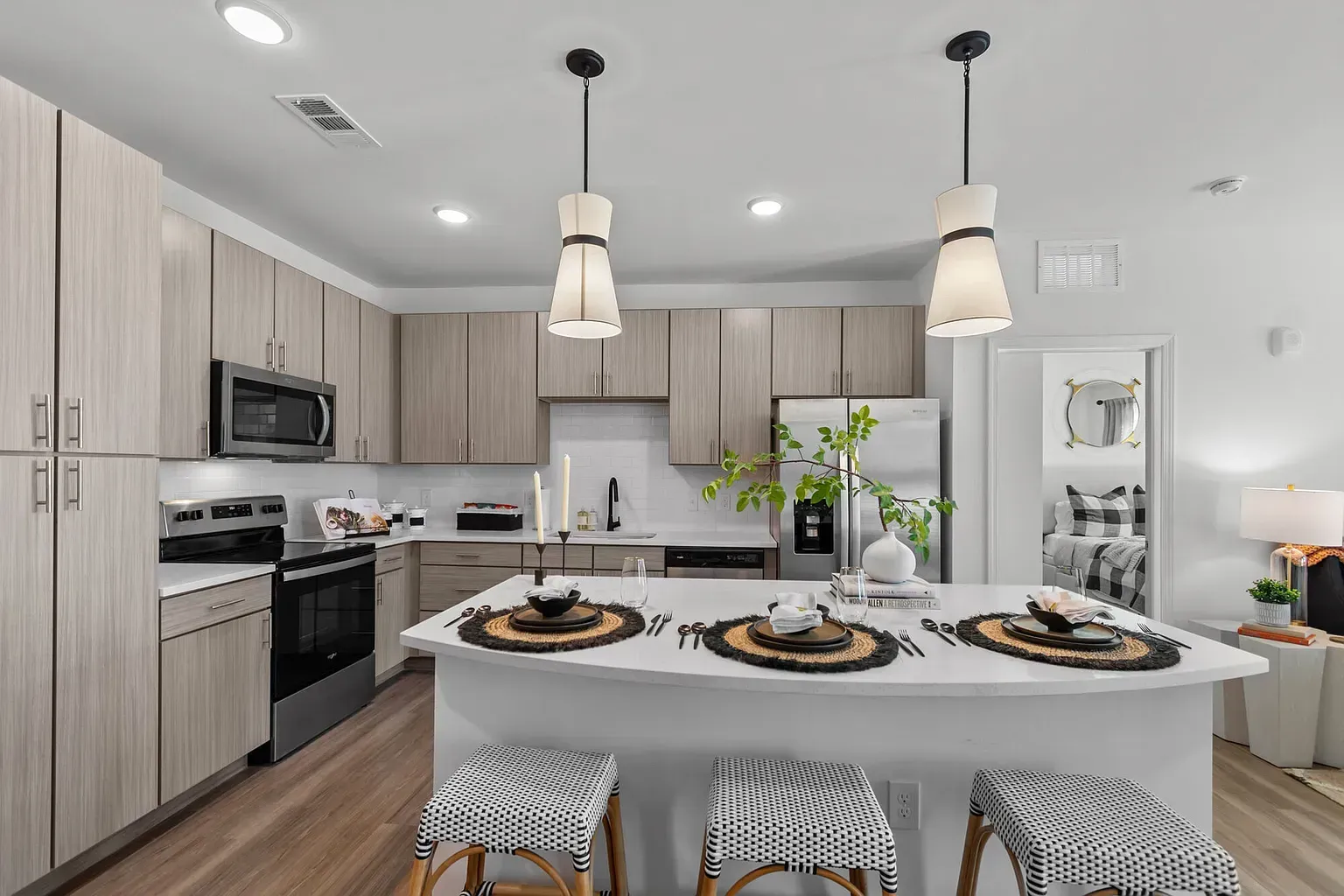 Modern kitchen with light wood cabinets, white countertops, island, and pendant lights.