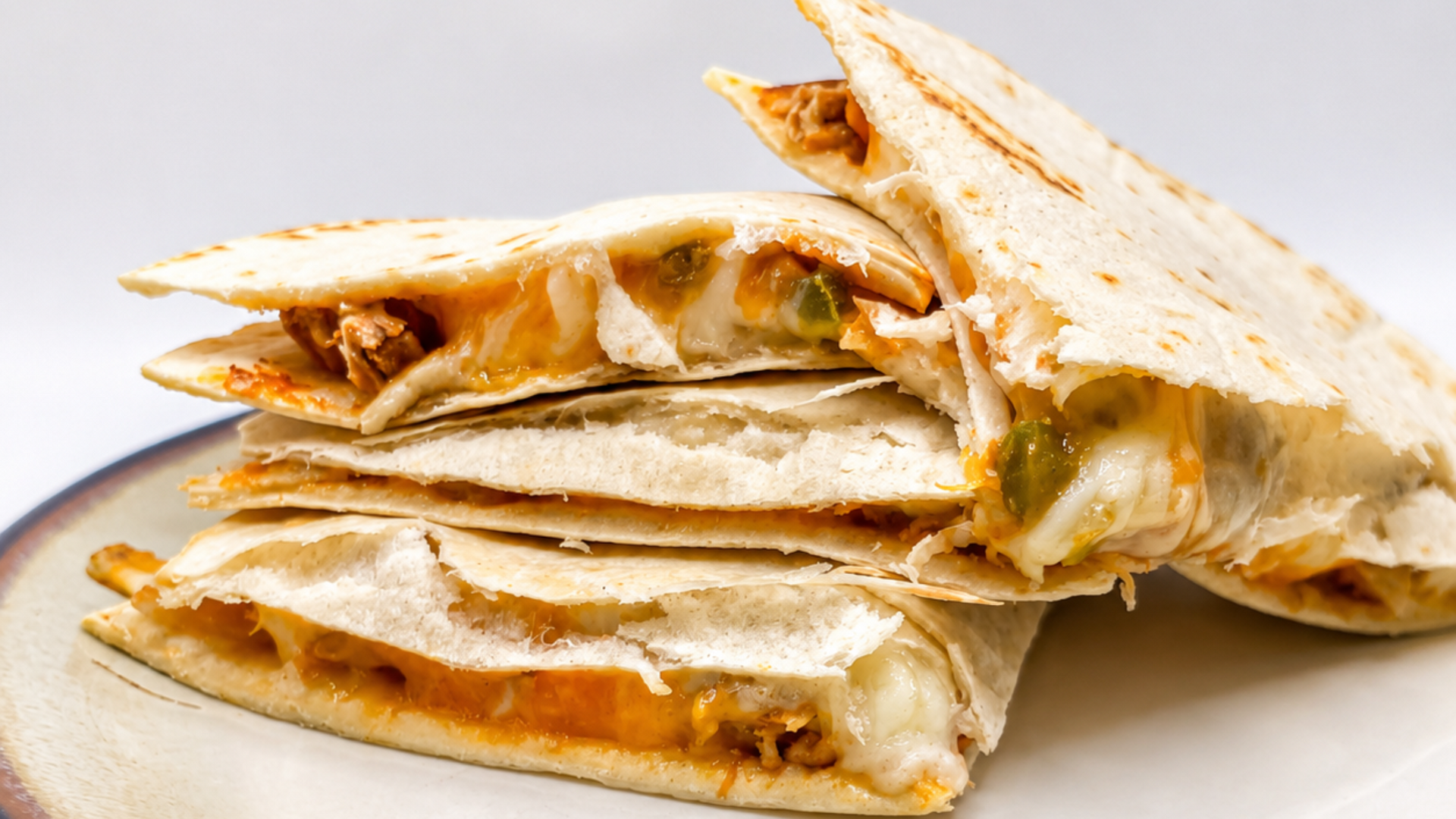 Quesadillas stacked on a plate; tortilla wraps filled with cheese and meat.