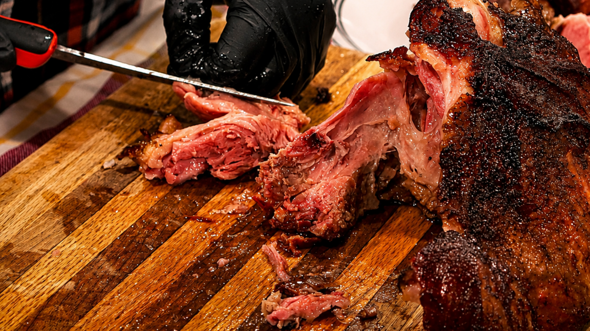 Sliced smoked brisket on a wooden cutting board with a carving knife and black gloves