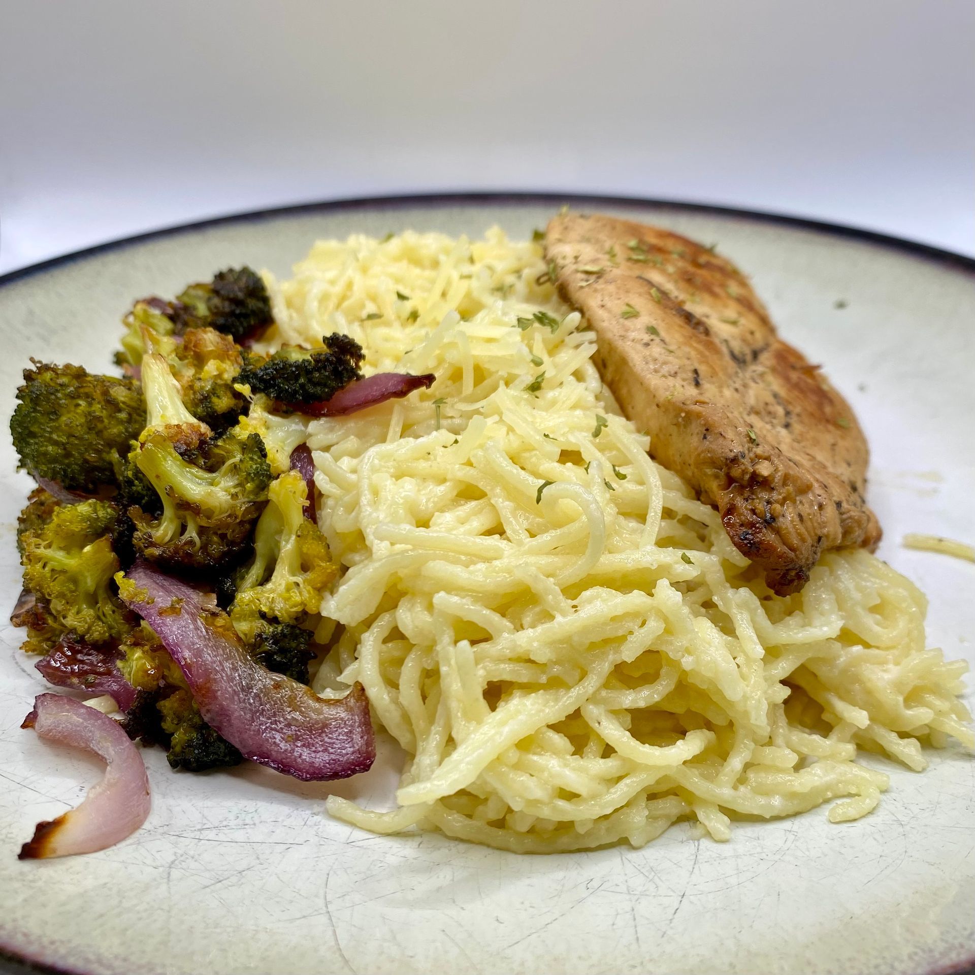 Plate of pasta, chicken, roasted broccoli and red onion.