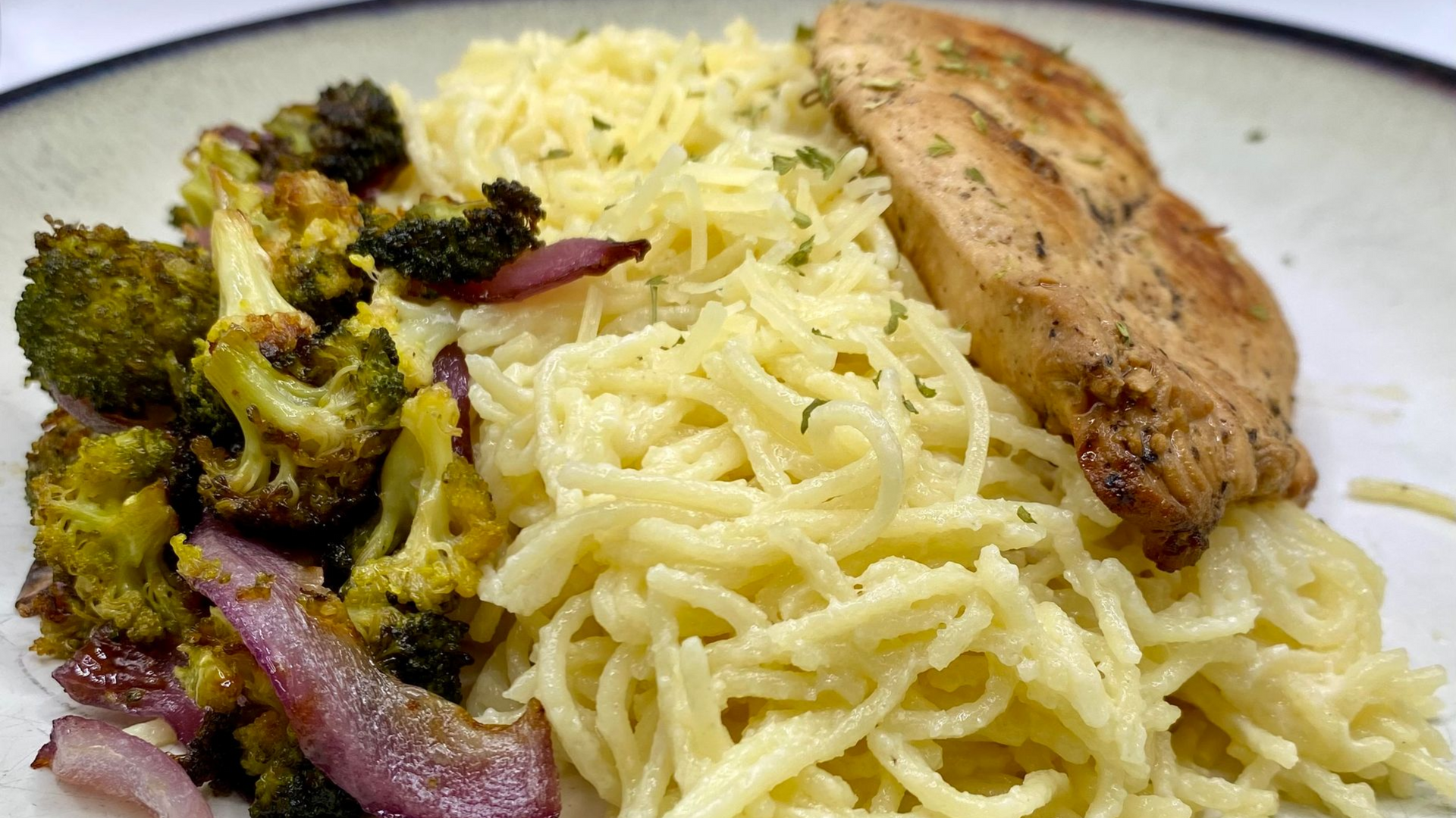 Plate of rice with roasted broccoli, red onions, and a grilled chicken breast