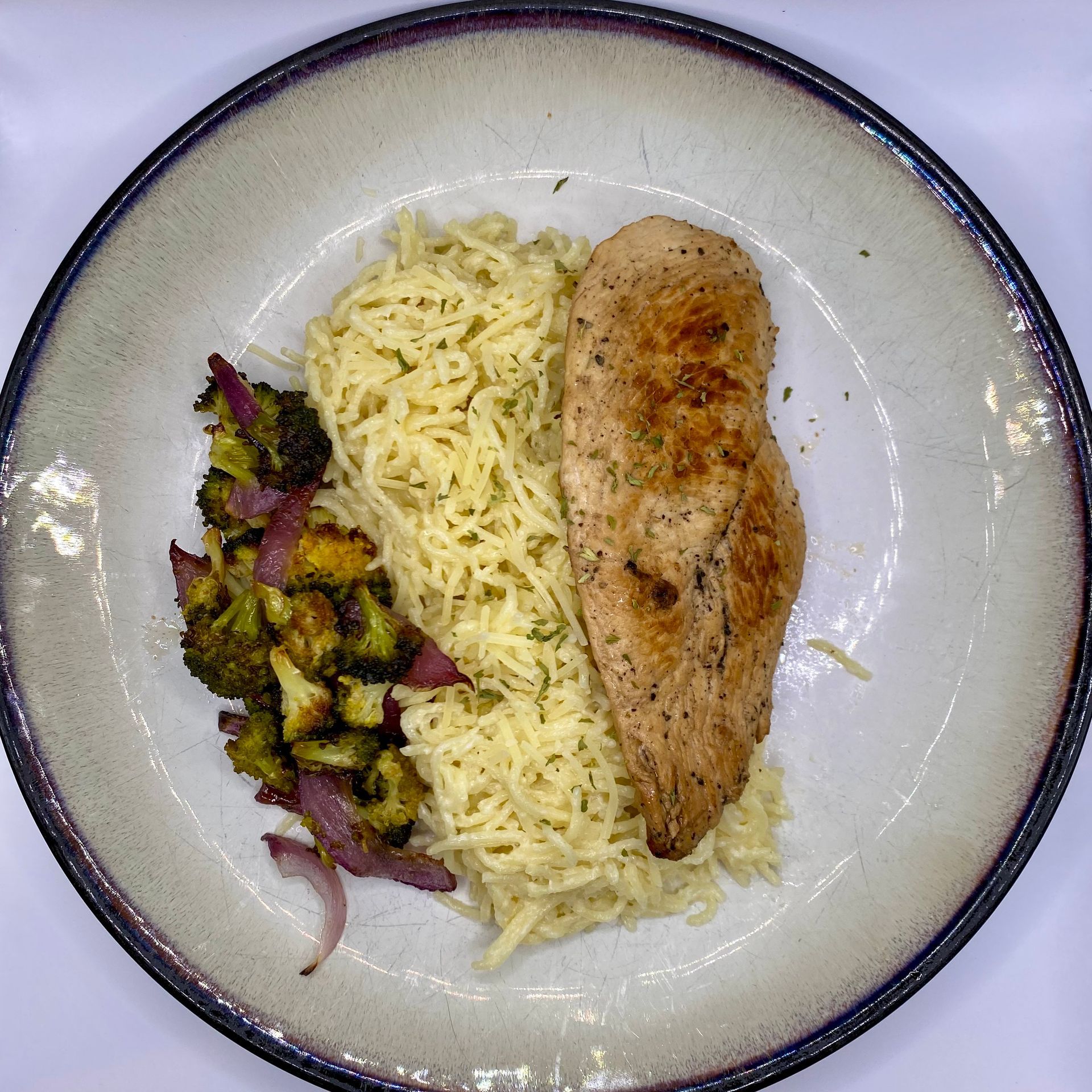 Plate with grilled chicken breast, rice, and roasted broccoli and red onion.