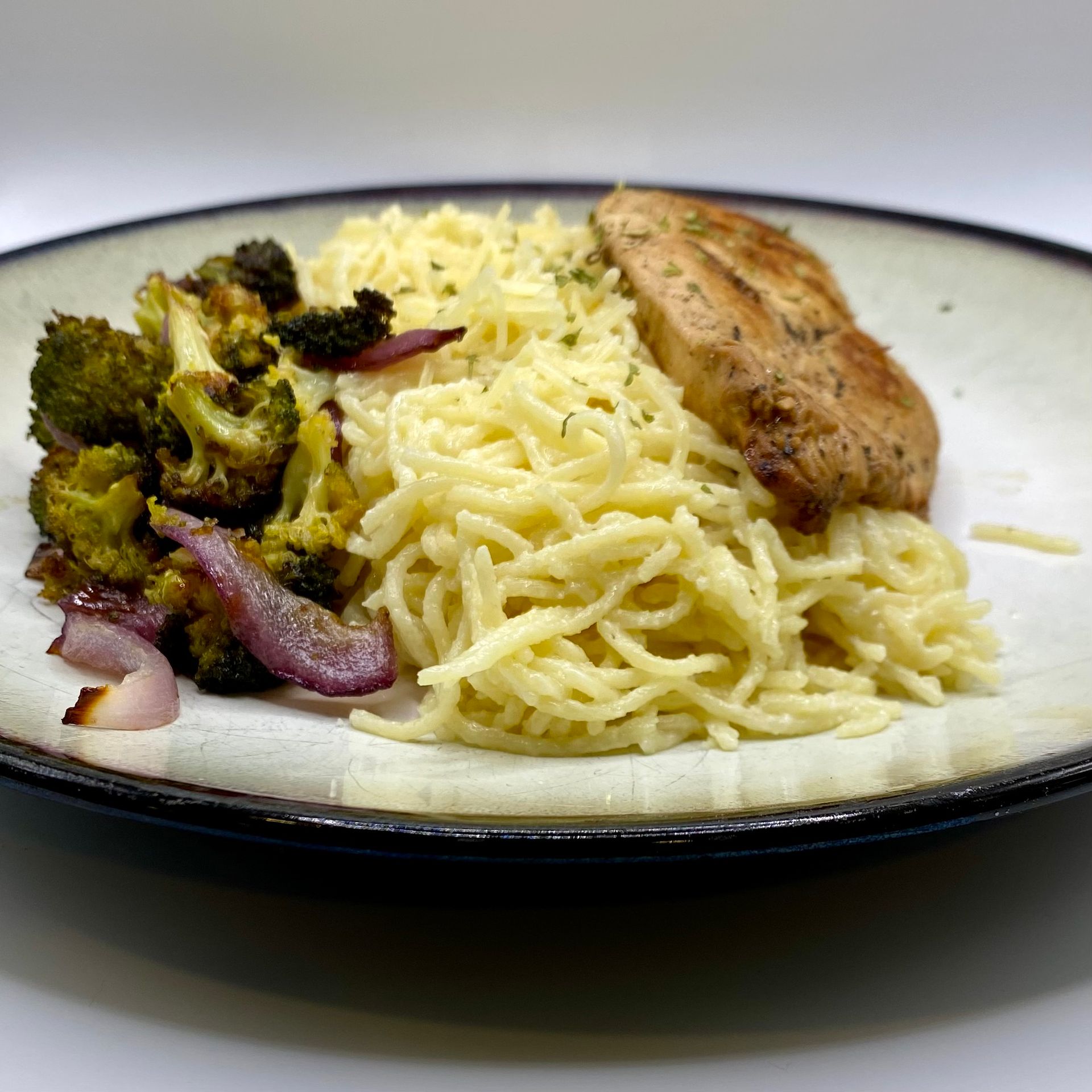 Plate of spaghetti, roasted broccoli and red onion, and a chicken breast.