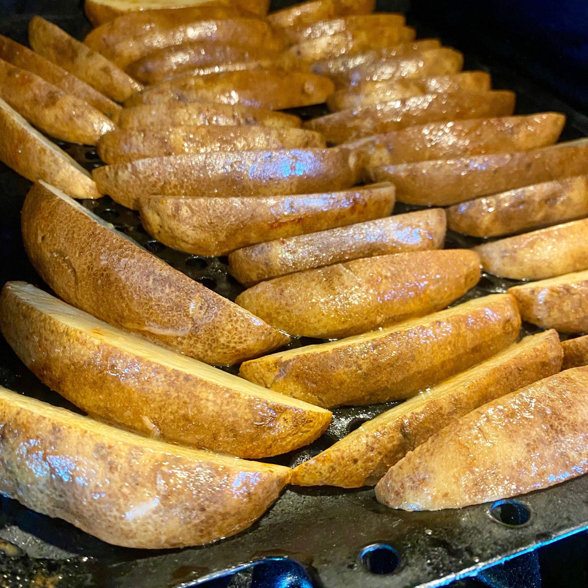 Golden brown potato wedges on a black grill.