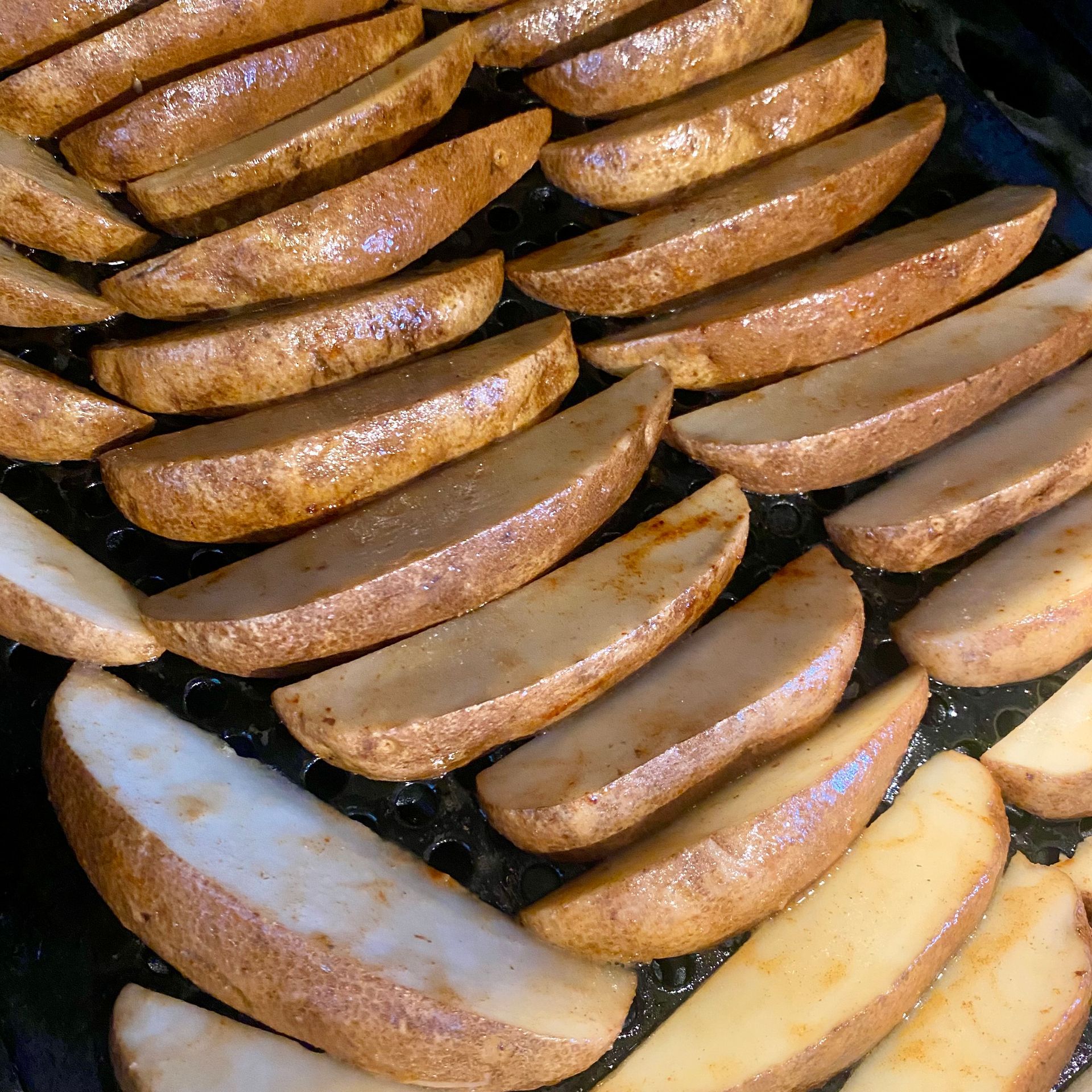 Golden brown potato wedges on a dark baking sheet, ready to eat.