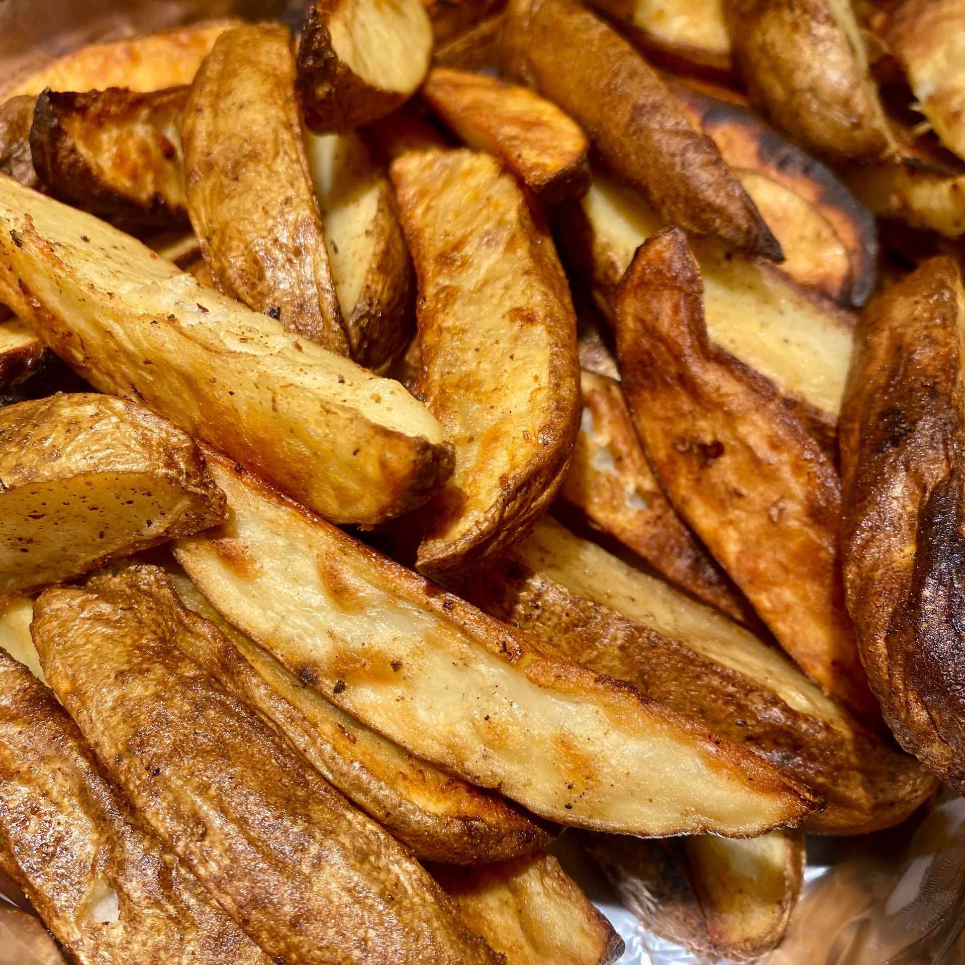 Close-up of golden-brown potato wedges, some slightly charred, in a bowl.