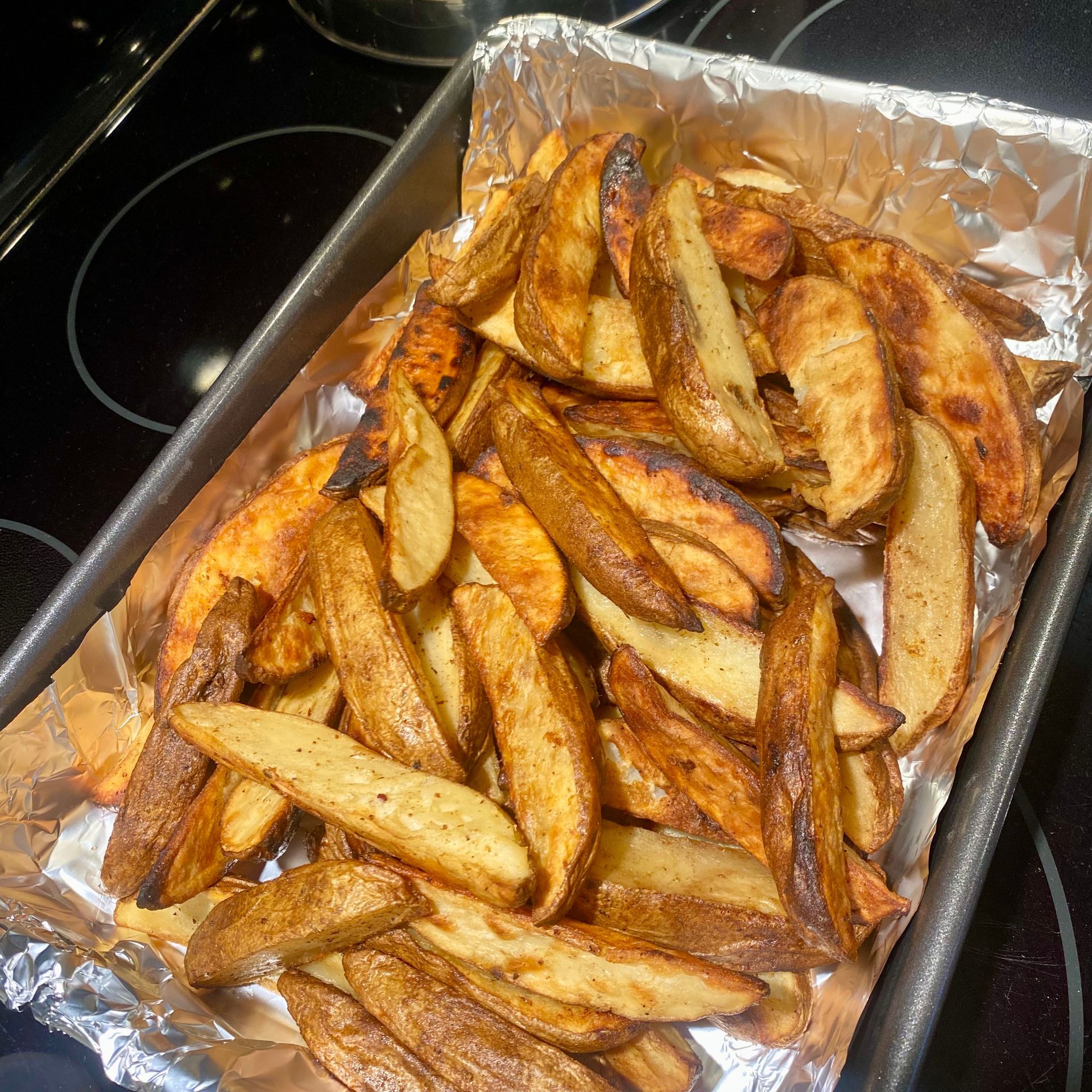 Crispy roasted potato wedges on a foil-lined baking sheet.