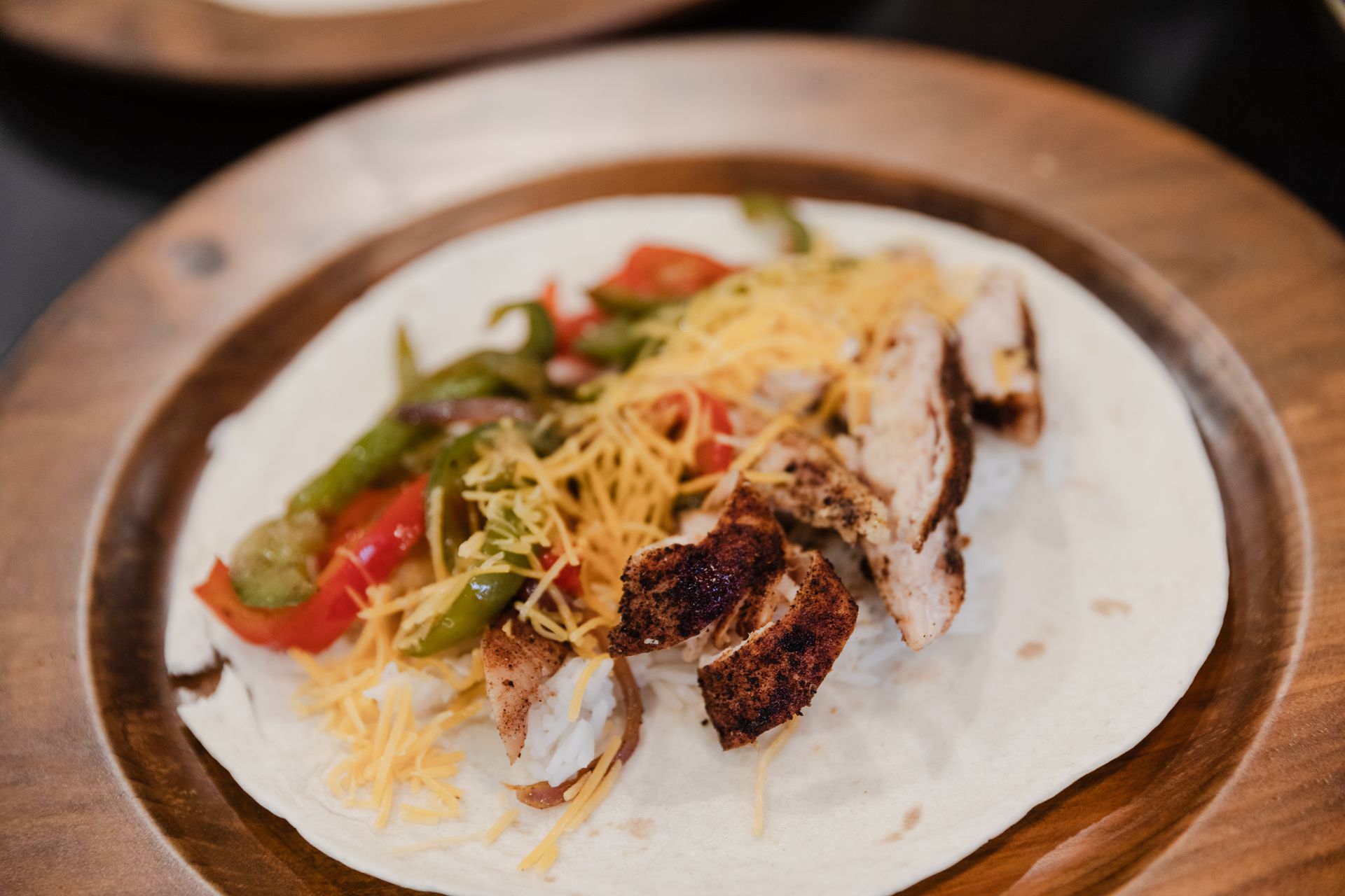 A close up of a tortilla with meat and vegetables on a wooden plate.