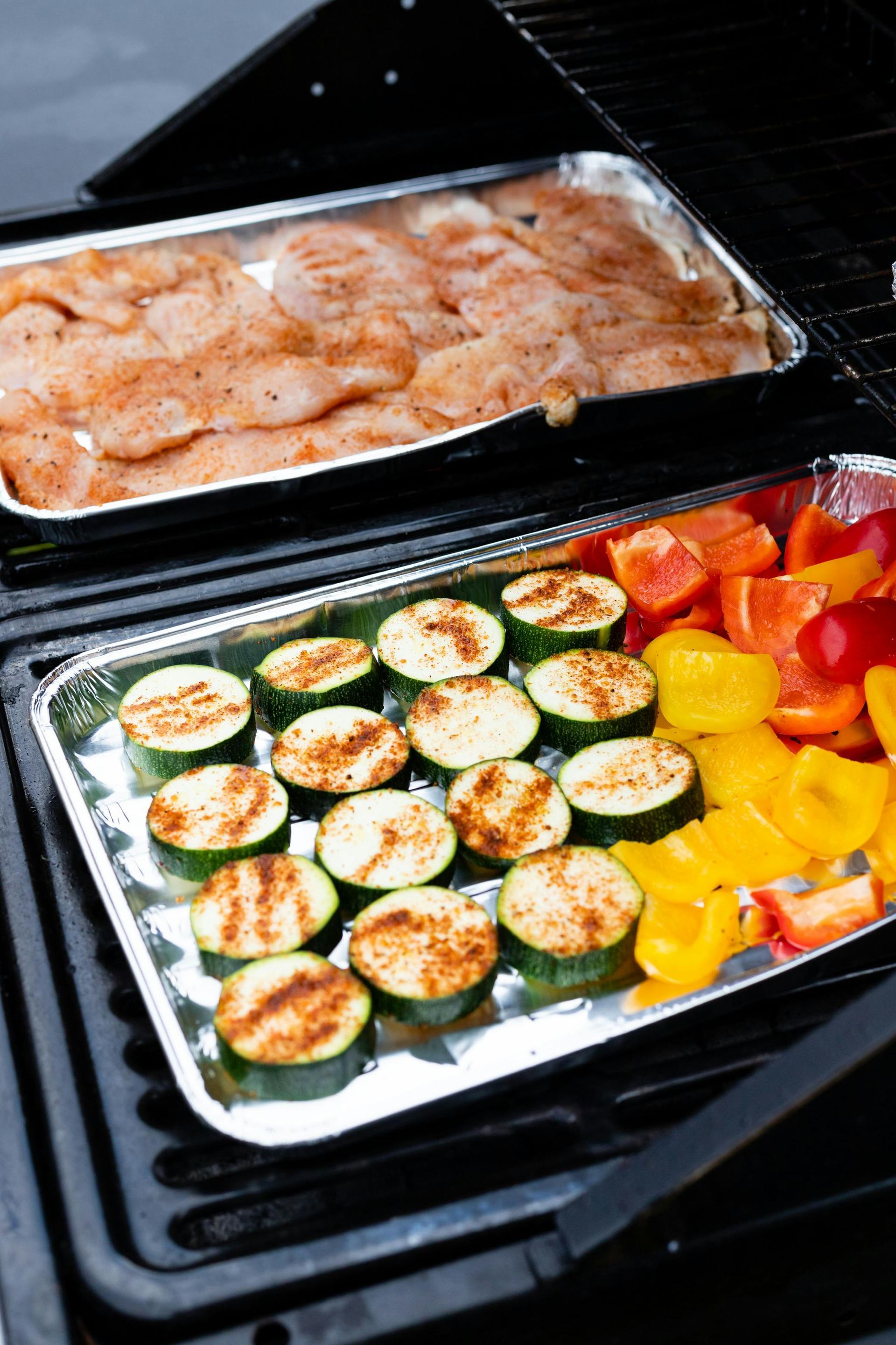 Trays of seasoned shrimp and grilled vegetables cooking on a barbecue grill
