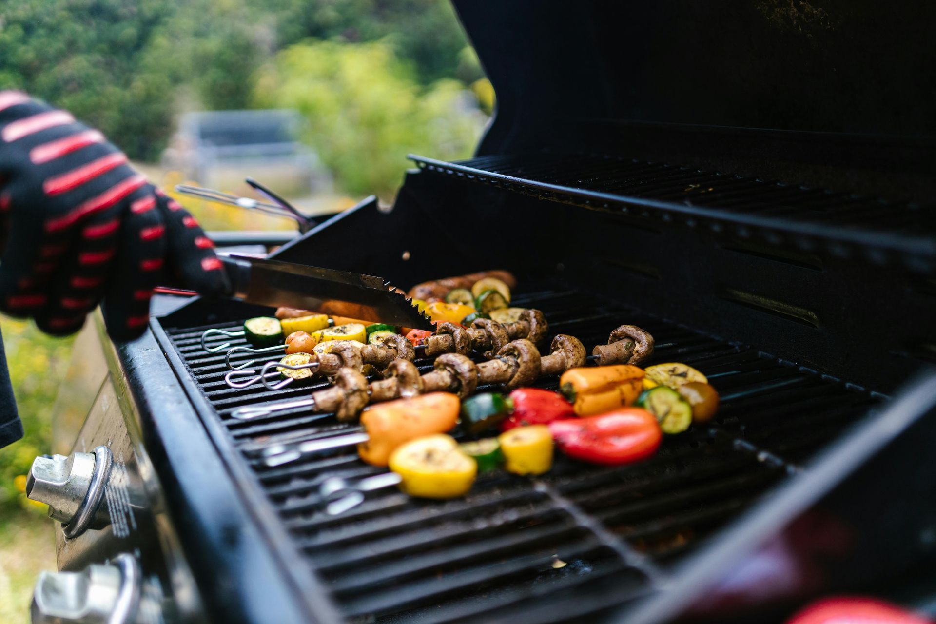 Person grilling vegetables and meat on an outdoor barbecue with colorful bell peppers and skewers
