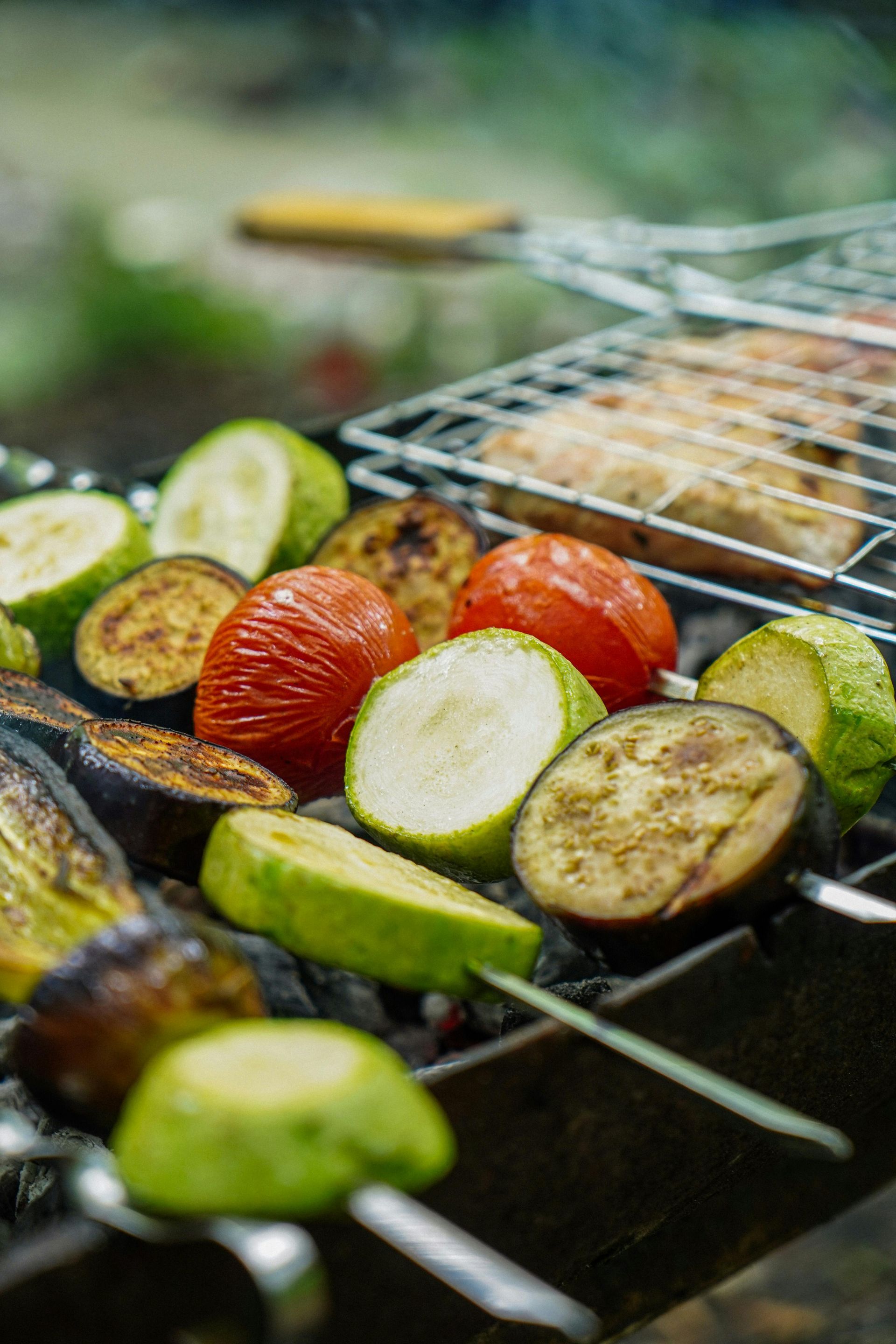 Vegetables grilling on a barbecue: zucchini, tomatoes, eggplant, and corn on a metal grate.