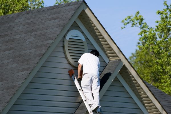 A man on a ladder paints the side of a house