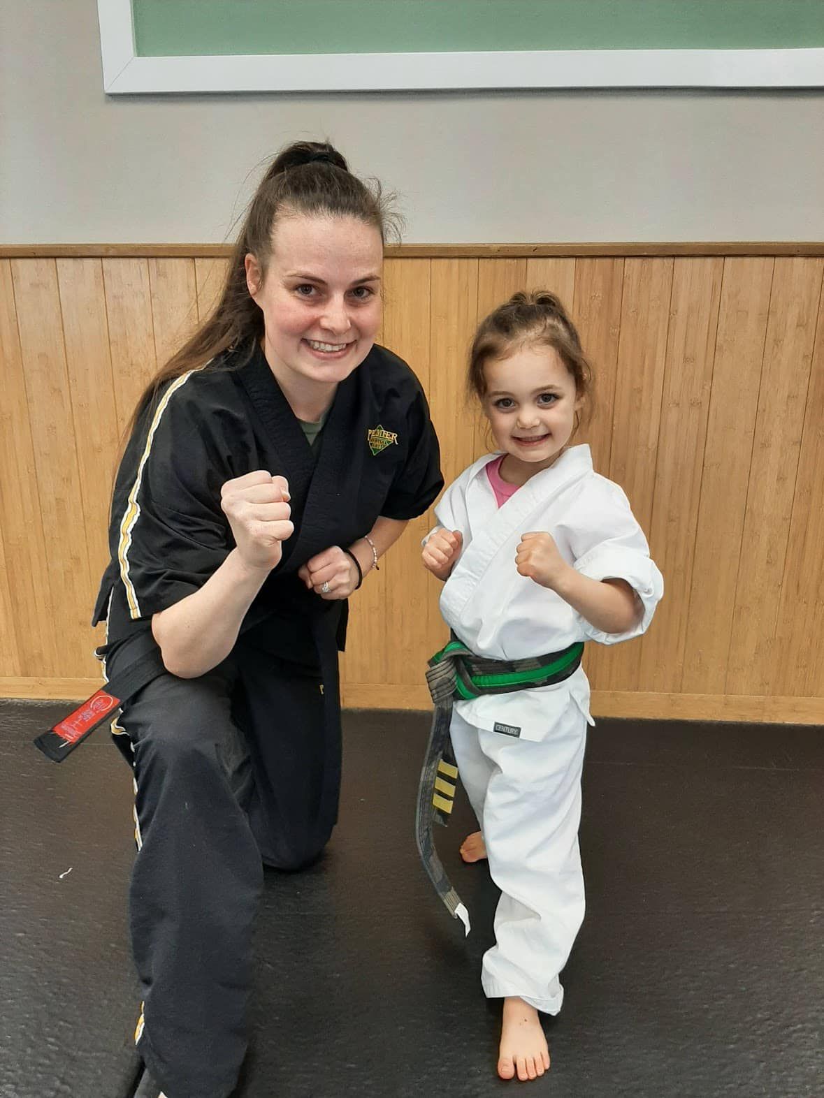 A woman is kneeling next to a little girl in a karate uniform.