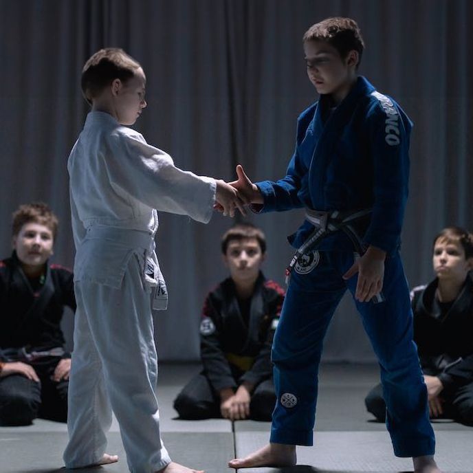 A man in a blue kimono is shaking hands with another man in a white kimono