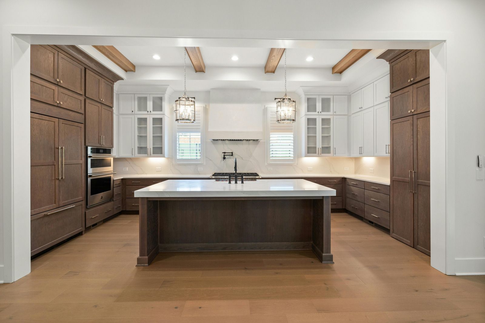 Modern kitchen with dark wood island, white cabinets, exposed ceiling beams, and light wood floors