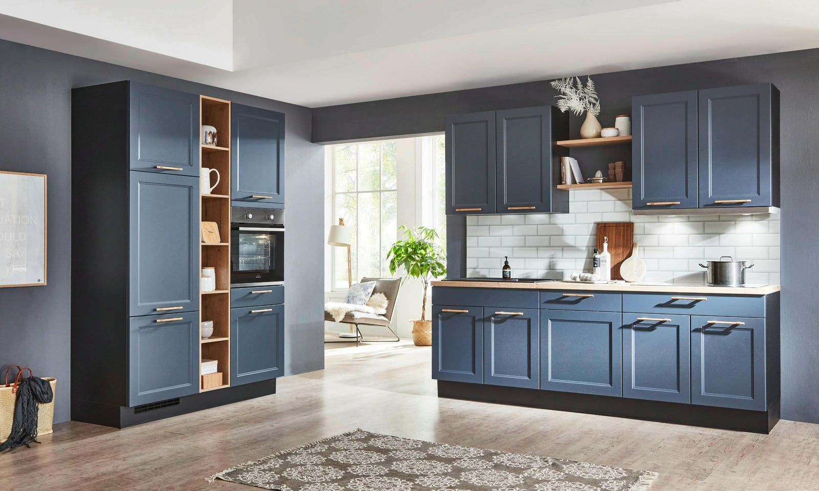 Modern kitchen with blue cabinets, stainless appliances, and a bright dining nook beyond the window.