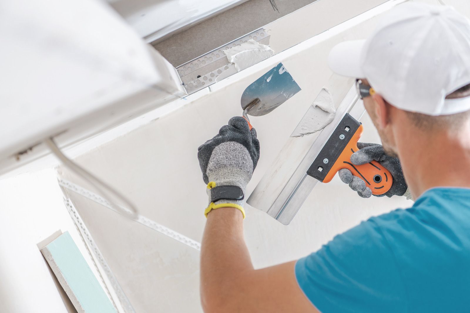 Worker painting a white ceiling with a roller and orange step ladder nearby