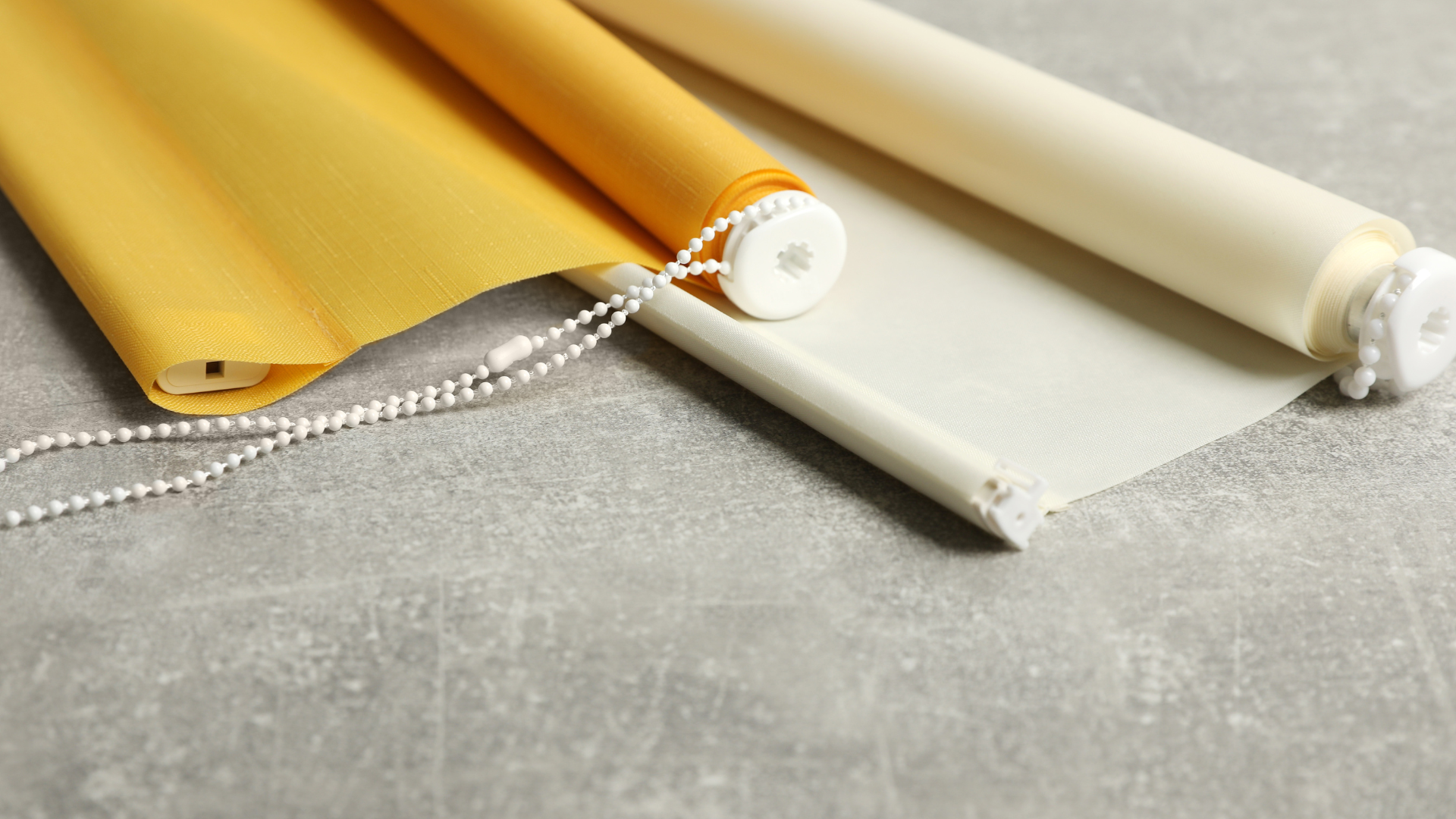 Three rolls of blinds with chains on a gray surface.