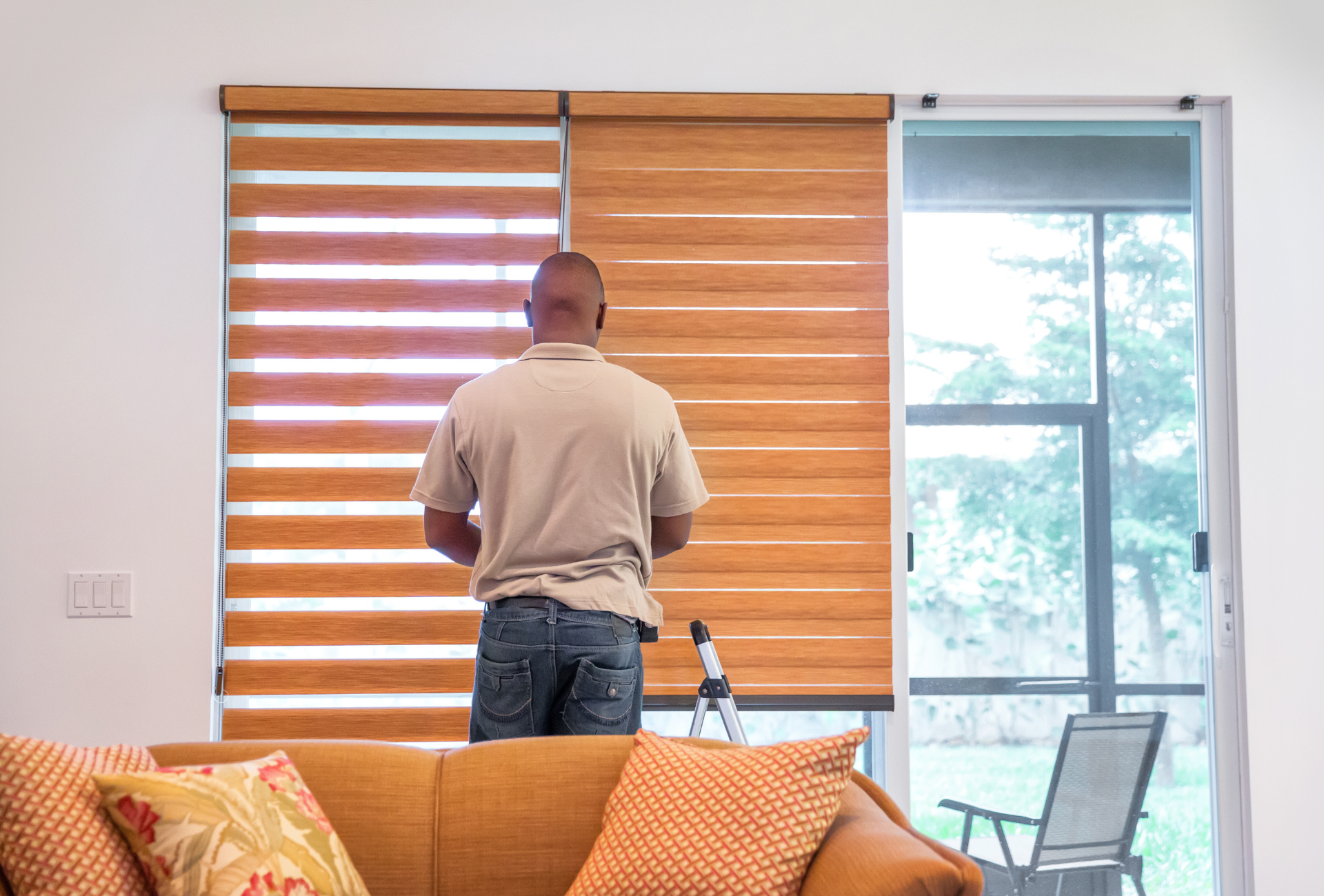 A man is installing blinds on a window in a living room.