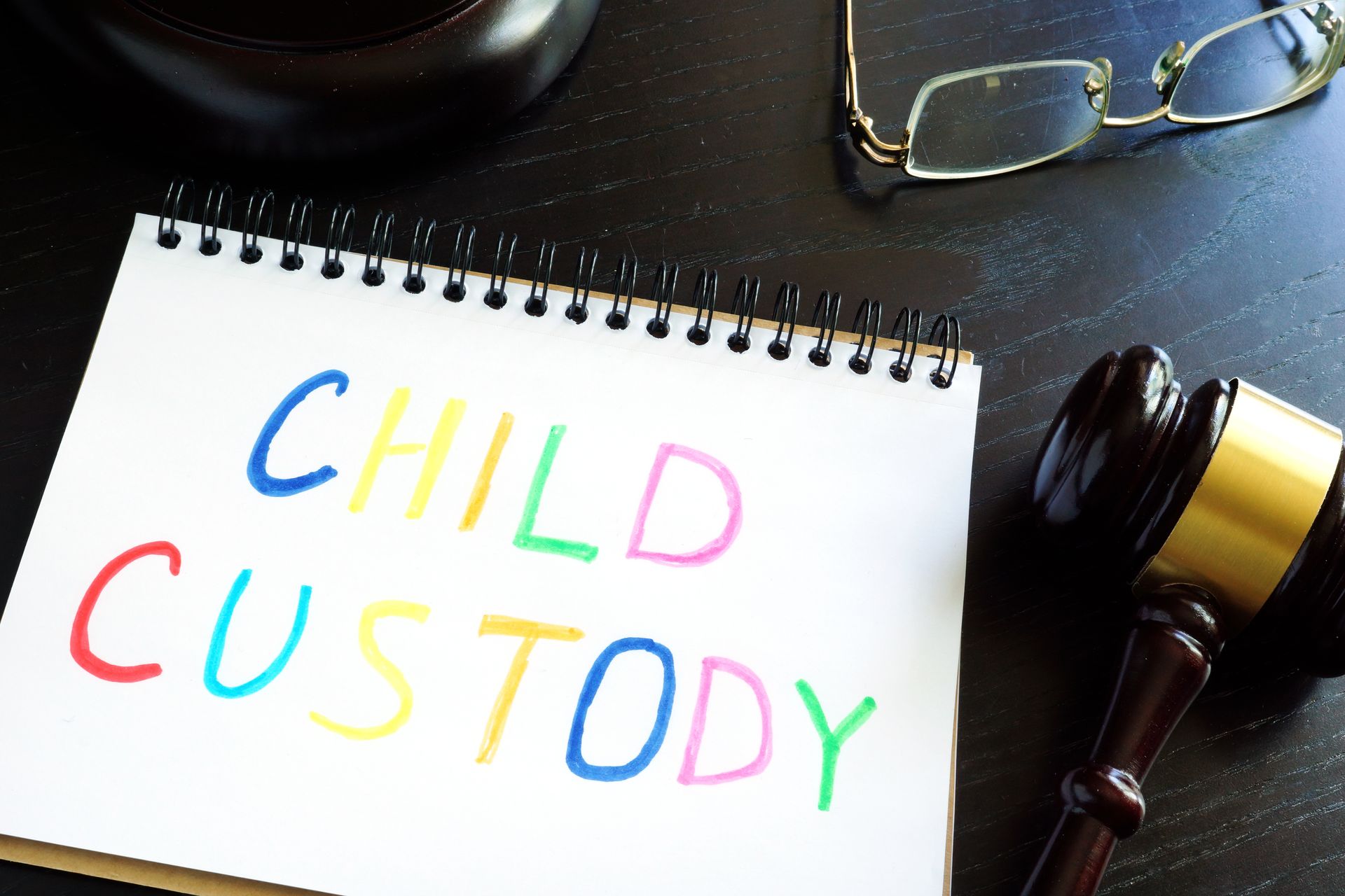 A notebook marked “Child Custody” sits beside a judge’s gavel and a pair of glasses. A notebook marked “Child Custody” sits beside a judge’s gavel and a pair of glasses.