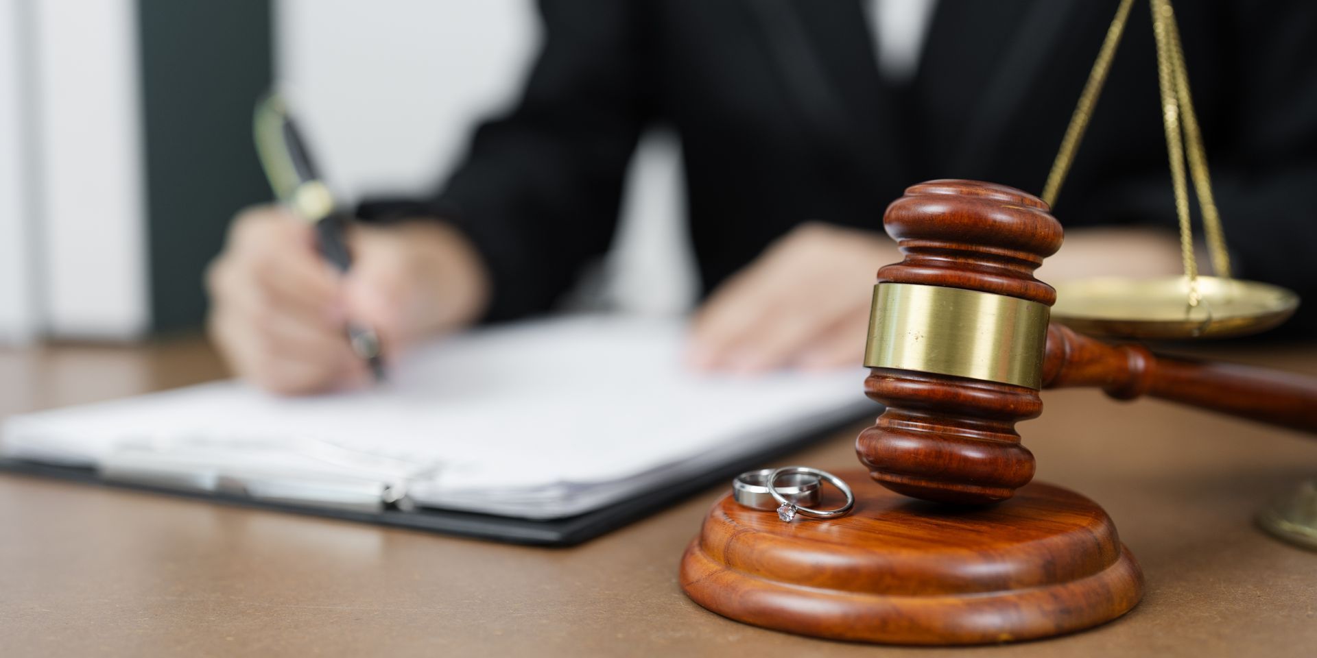 Experienced divorce attorney signing legal documents beside a gavel, scales of justice, and wedding rings.