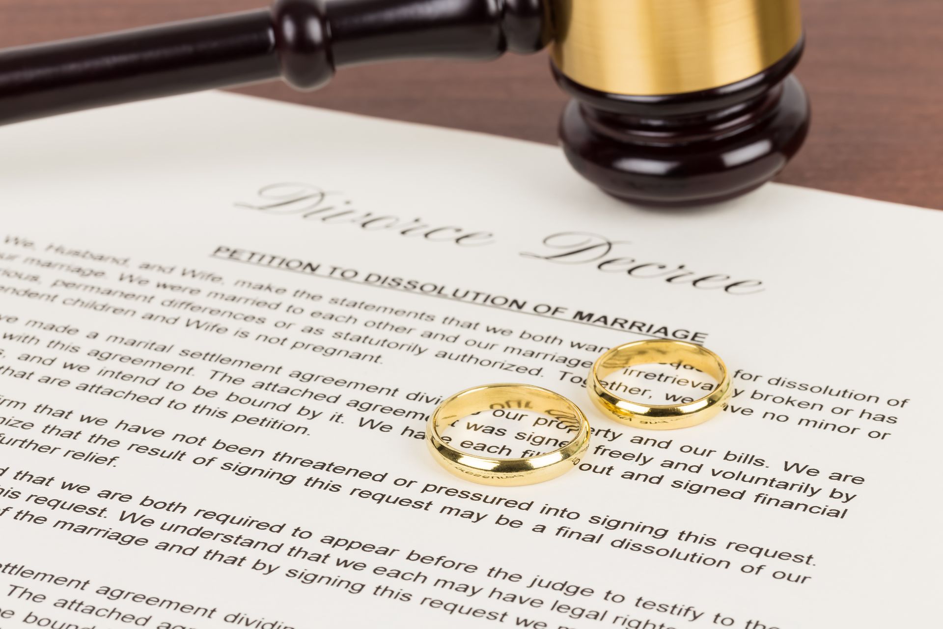A gavel and two wedding rings placed on a divorce decree document. A gavel and two wedding rings placed on a divorce decree document.