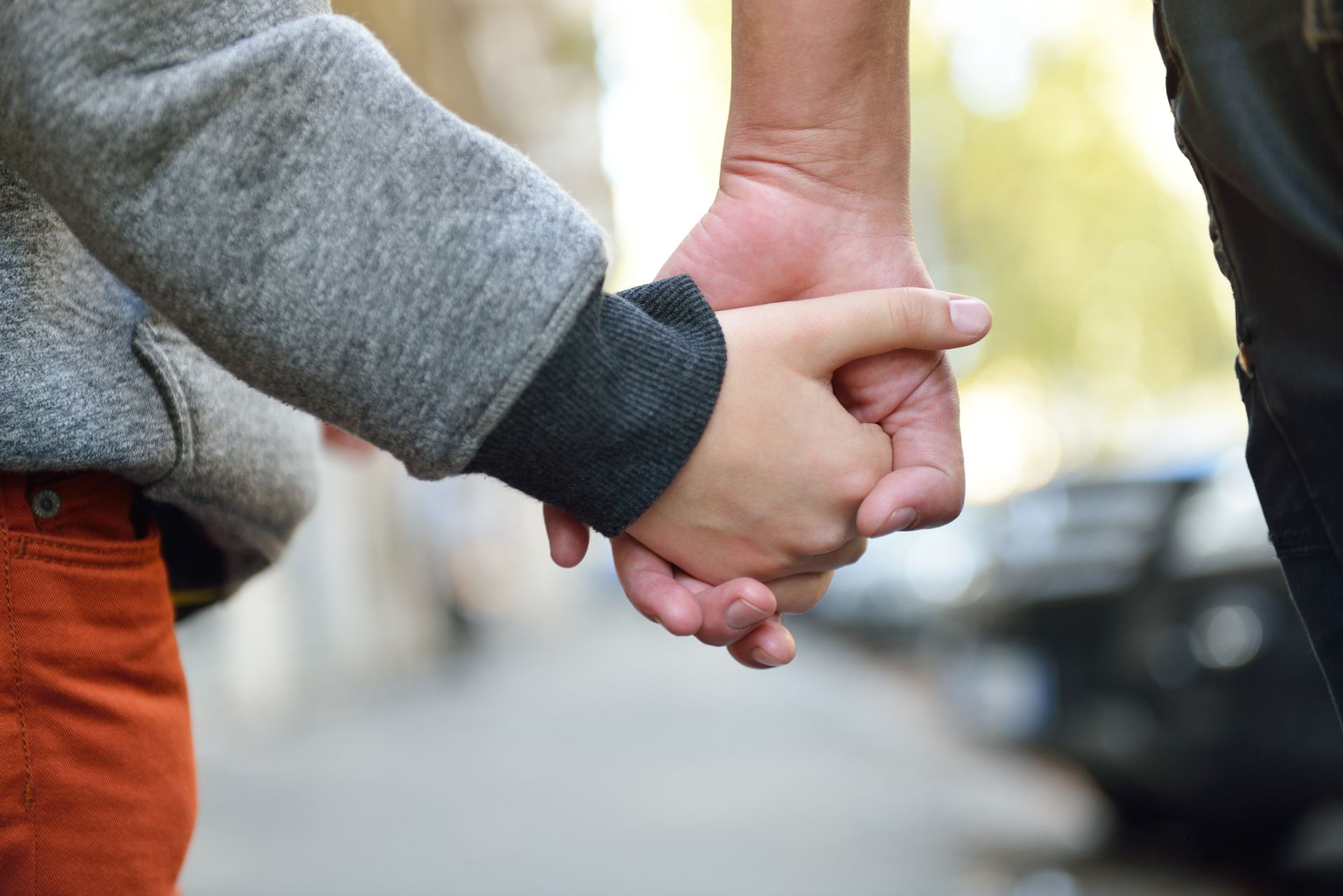 An adult and child walk together while holding hands on a sidewalk. An adult and child walk together while holding hands on a sidewalk.